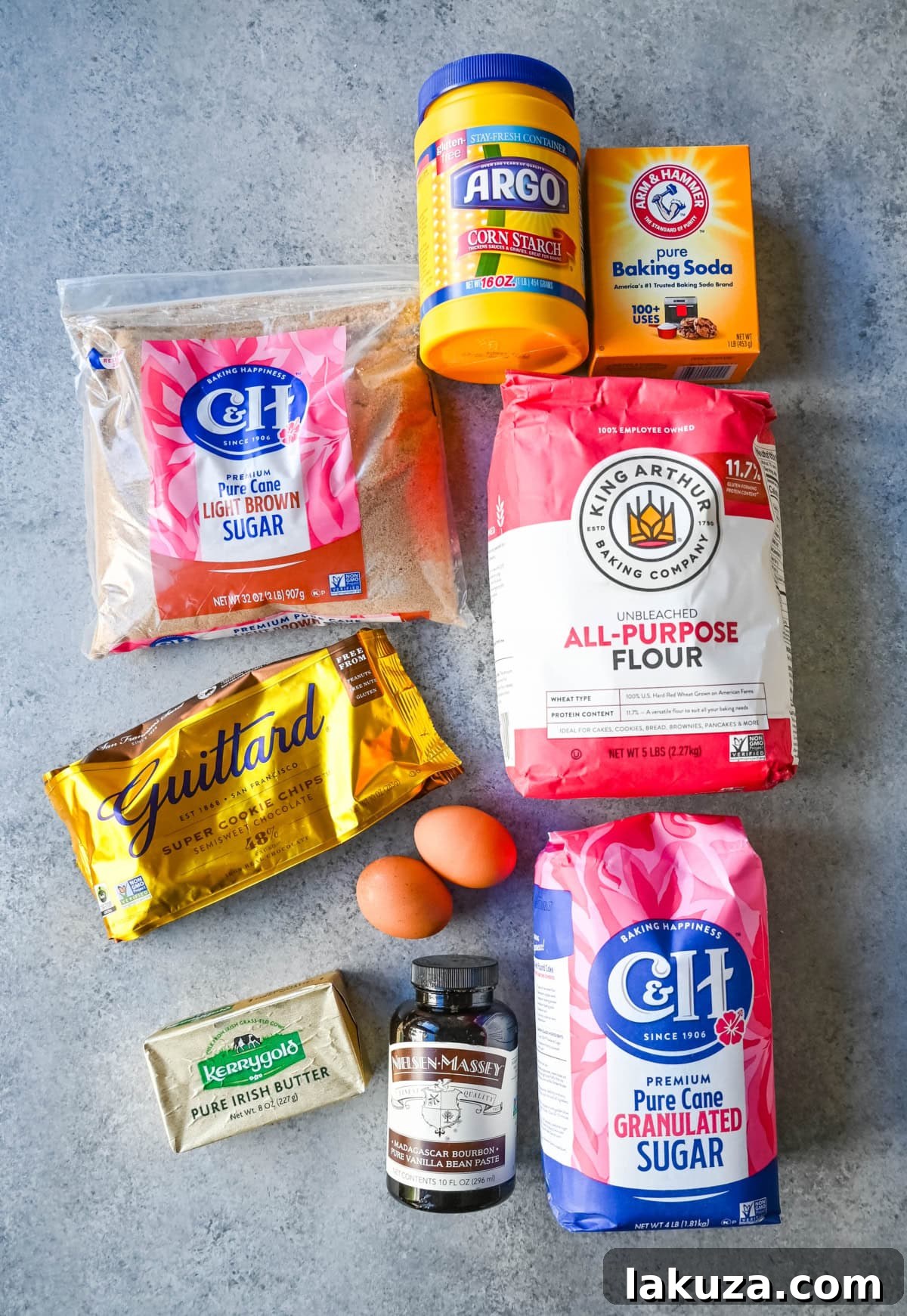 A collection of expensive, brand-name ingredients for chocolate chip cookies, including Guittard chocolate chips, Nielsen-Massey vanilla paste, Kerrygold butter, C&H sugar, and King Arthur Flour.