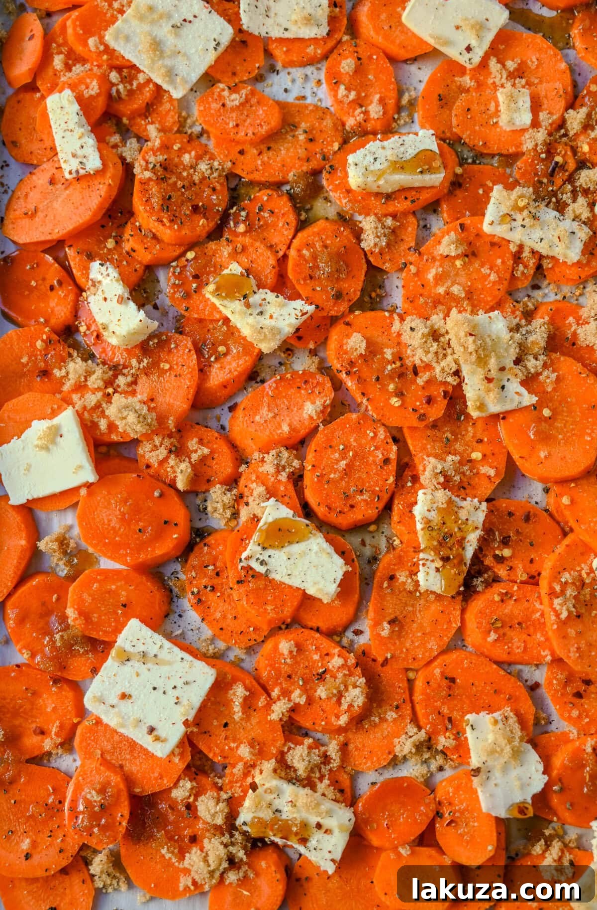 Roasted Maple Glazed Carrots spread on a parchment-lined baking sheet, glistening with glaze, and ready to be placed in the oven for roasting.