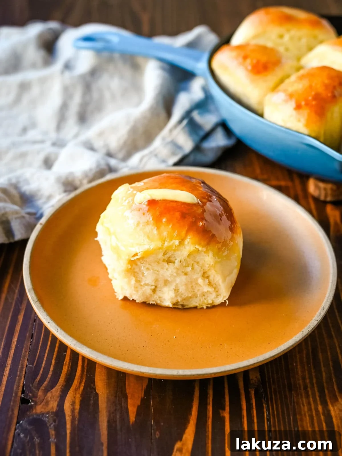 Pillowy Japanese Milk Buns 4 A single homemade Japanese milk bread dinner roll resting on a plate, showcasing its golden exterior and promise of an exceptionally soft and tender interior, achieved with the tangzhong technique.