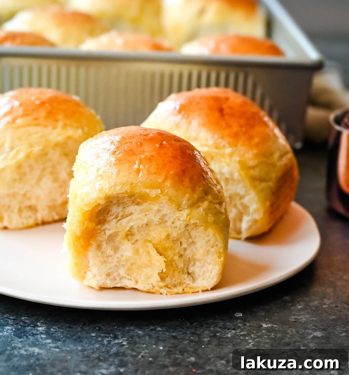 Pillowy Japanese Milk Buns 7 A freshly baked homemade dinner roll on a ceramic plate, golden-brown and promising extreme softness. This Japanese milk bread roll is a testament to the special tangzhong technique.