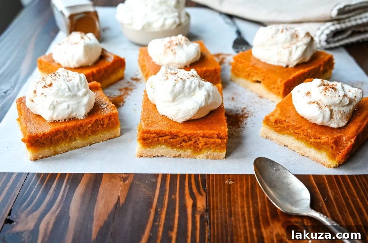 A close-up of a single pumpkin pie bar with a perfect shortbread crust, creamy filling, and a delicate swirl of whipped cream.