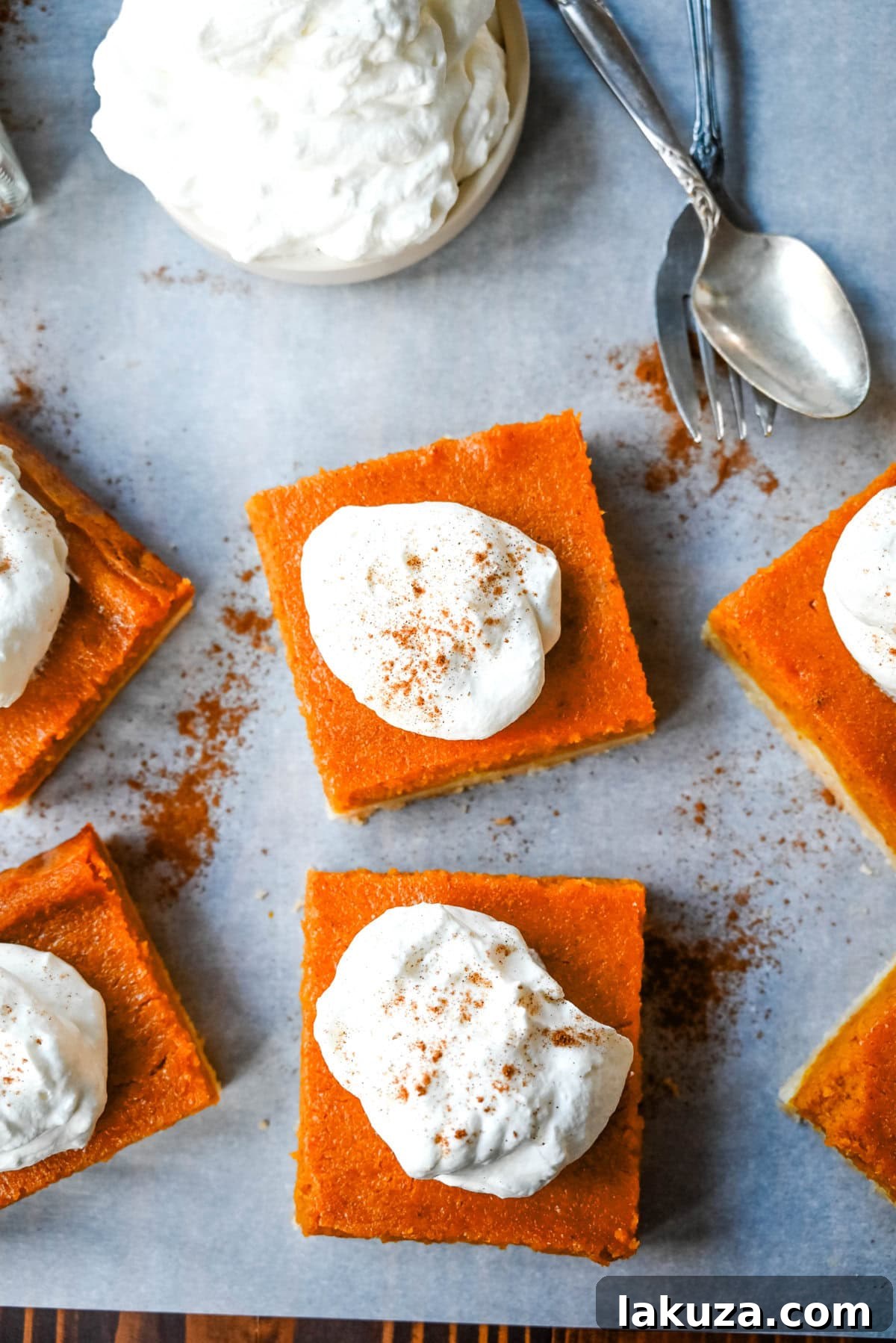 Several pumpkin pie bars garnished with whipped cream and cinnamon sit on a rustic wooden board, ready for a fall gathering.
