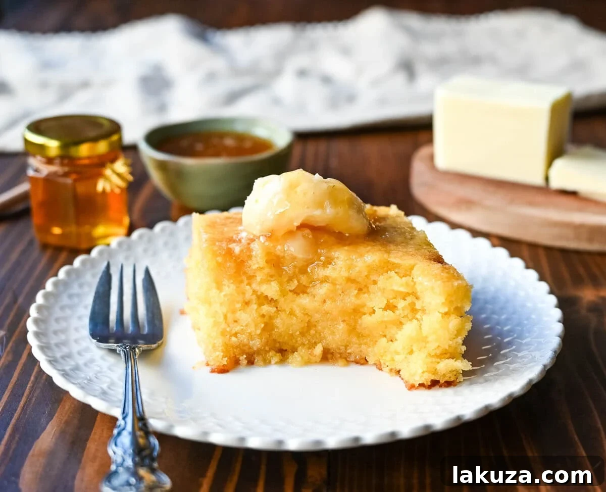 Southern Soul Cornbread 3 A delectable slice of moist cornbread, adorned with a generous swirl of golden honey butter, showcasing its tender crumb.