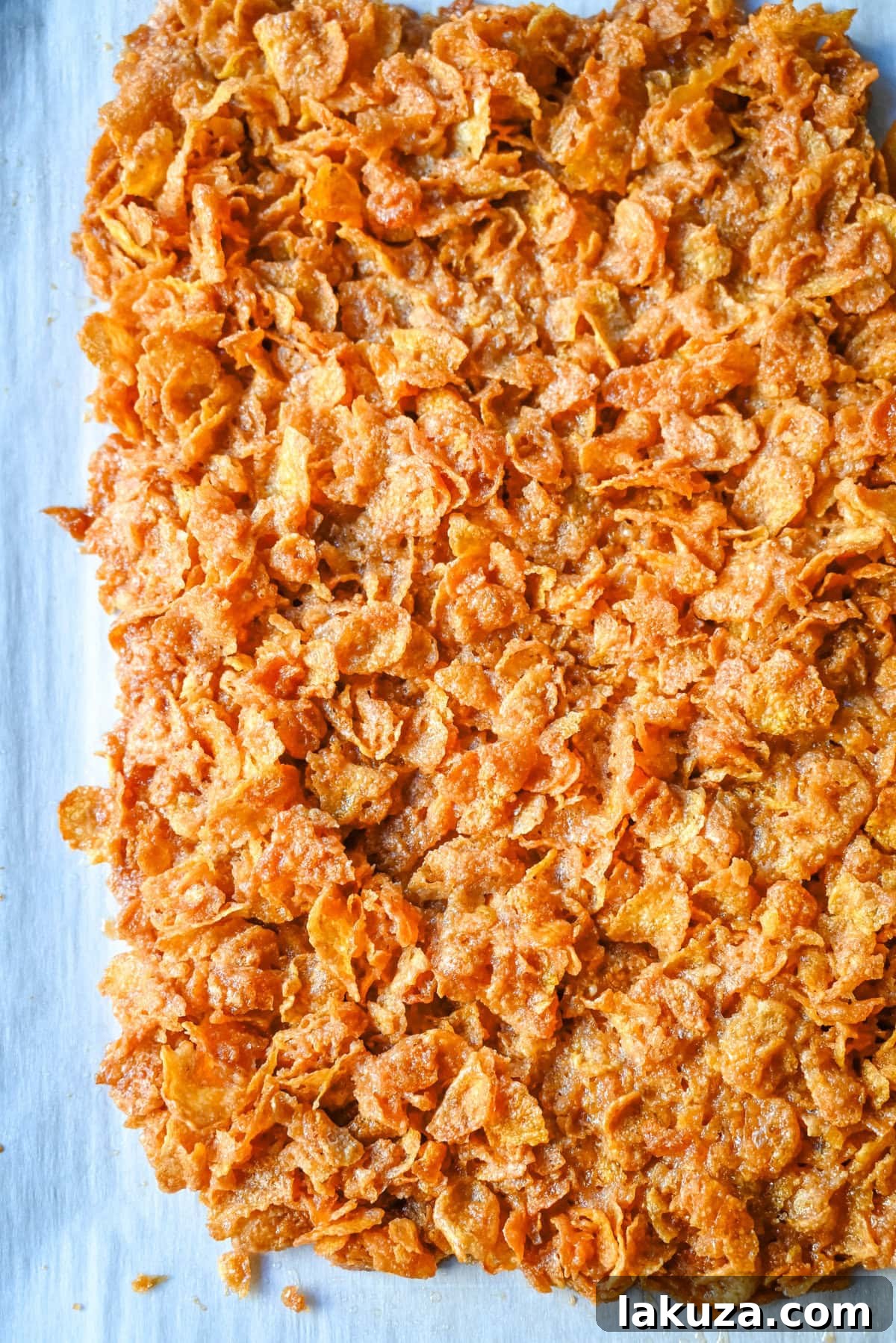 Butter and brown sugar caramel mixture being poured over cornflakes on a baking sheet, ready for baking.