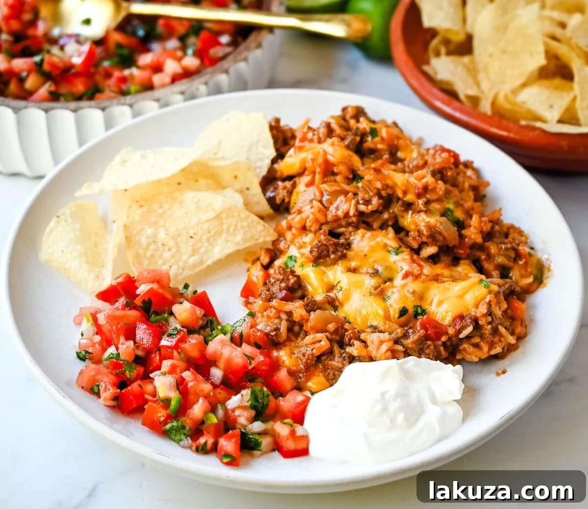 A serving of Cheesy Taco Rice Skillet in a bowl, topped with sour cream and cilantro, with a large skillet blurred in the background, highlighting its deliciousness.