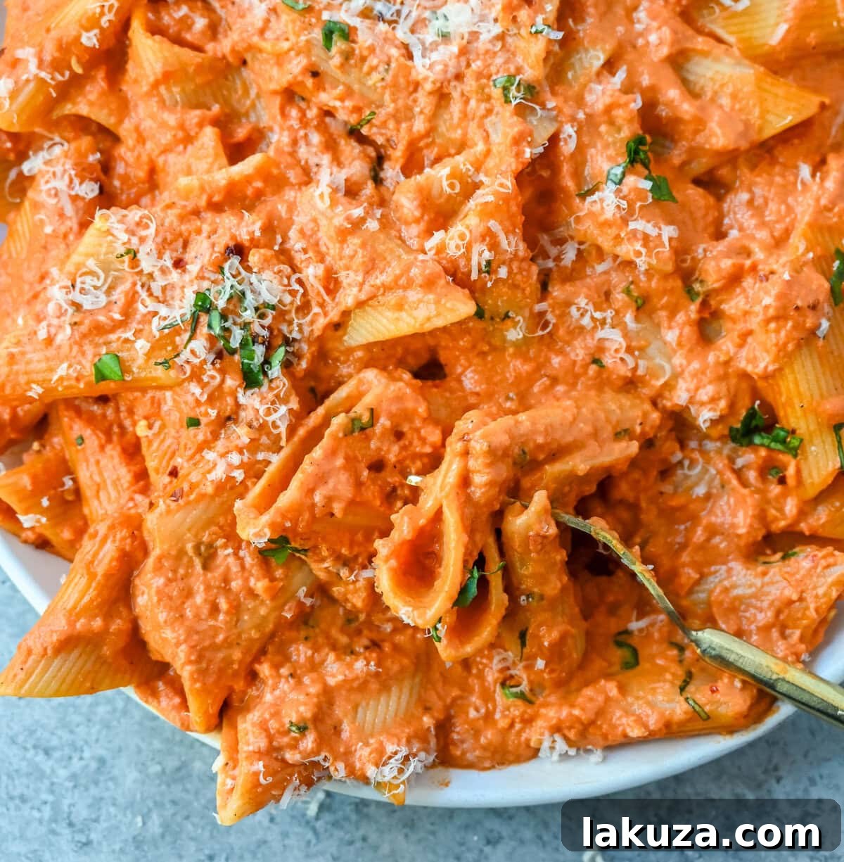 Cooked penne pasta being gently tossed into a rich, steaming vodka sauce within a large, inviting skillet, creating a perfect blend of flavors.