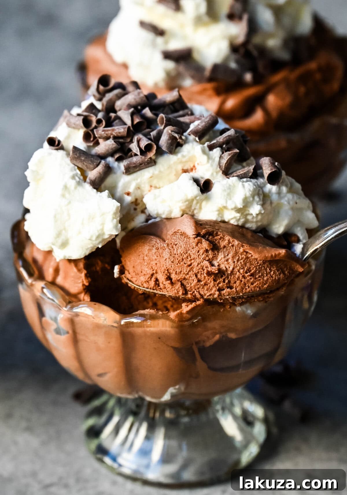 A decadent chocolate mousse served in elegant glasses, topped with a dollop of whipped cream and a single fresh raspberry, embodying gourmet simplicity.
