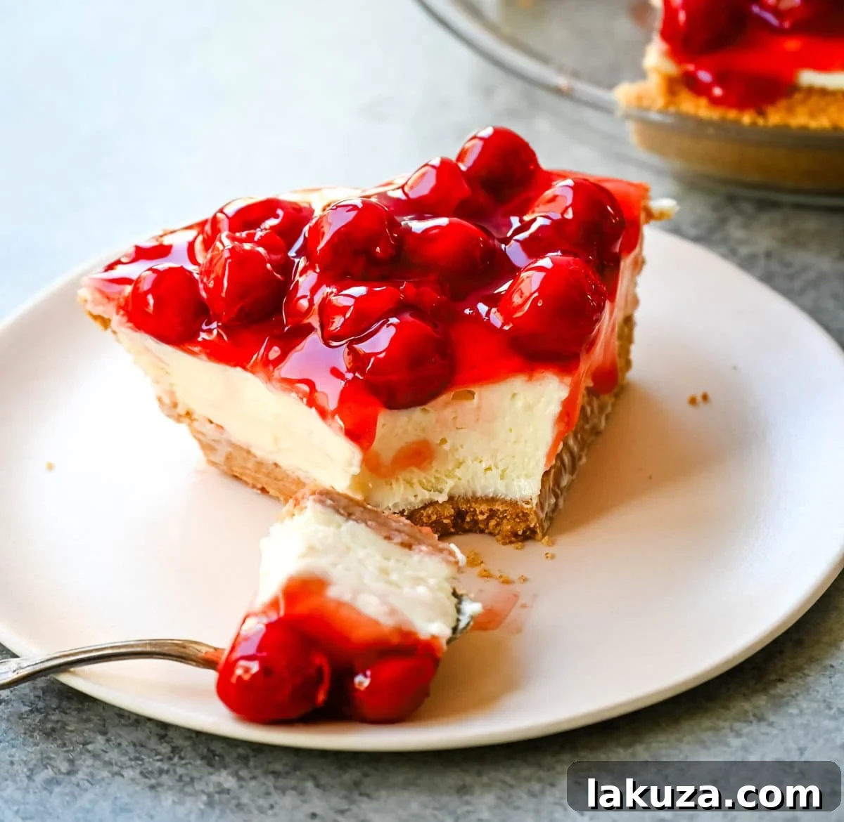 Dreamy No-Bake Cheesecake with Sweetened Condensed Milk 4 A slice of No-Bake Cheesecake with cherry topping being served, showing the distinct layers of crust and filling.