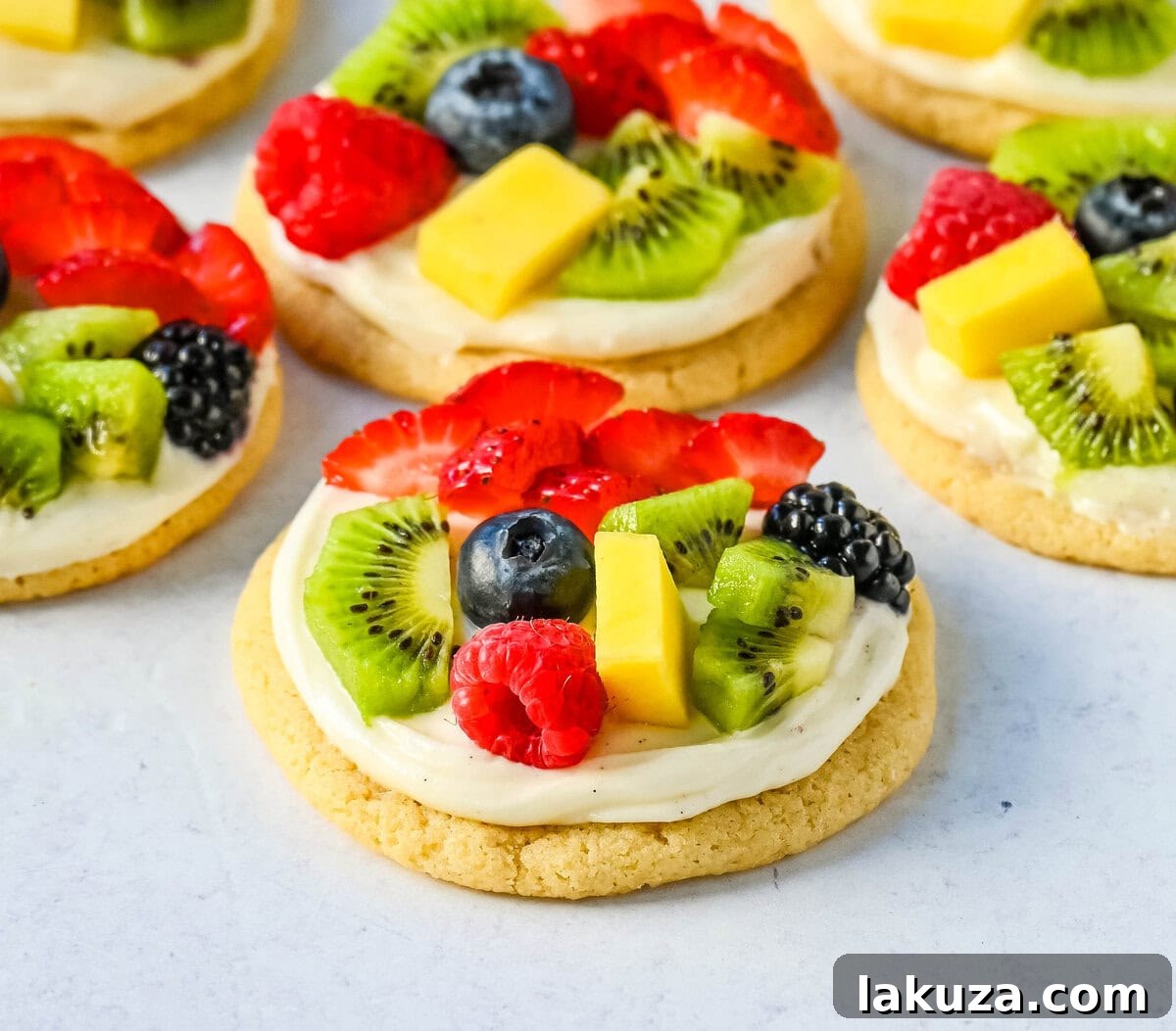 A close-up of a fruit pizza cookie topped with kiwi, blueberries, and raspberries, showcasing the creamy frosting and soft cookie base.