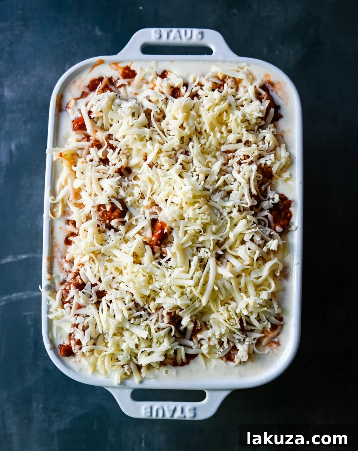 Detailed shot of assembling layers of meat lasagna with bechamel sauce, cheese, and pasta in a baking dish, showcasing the process.