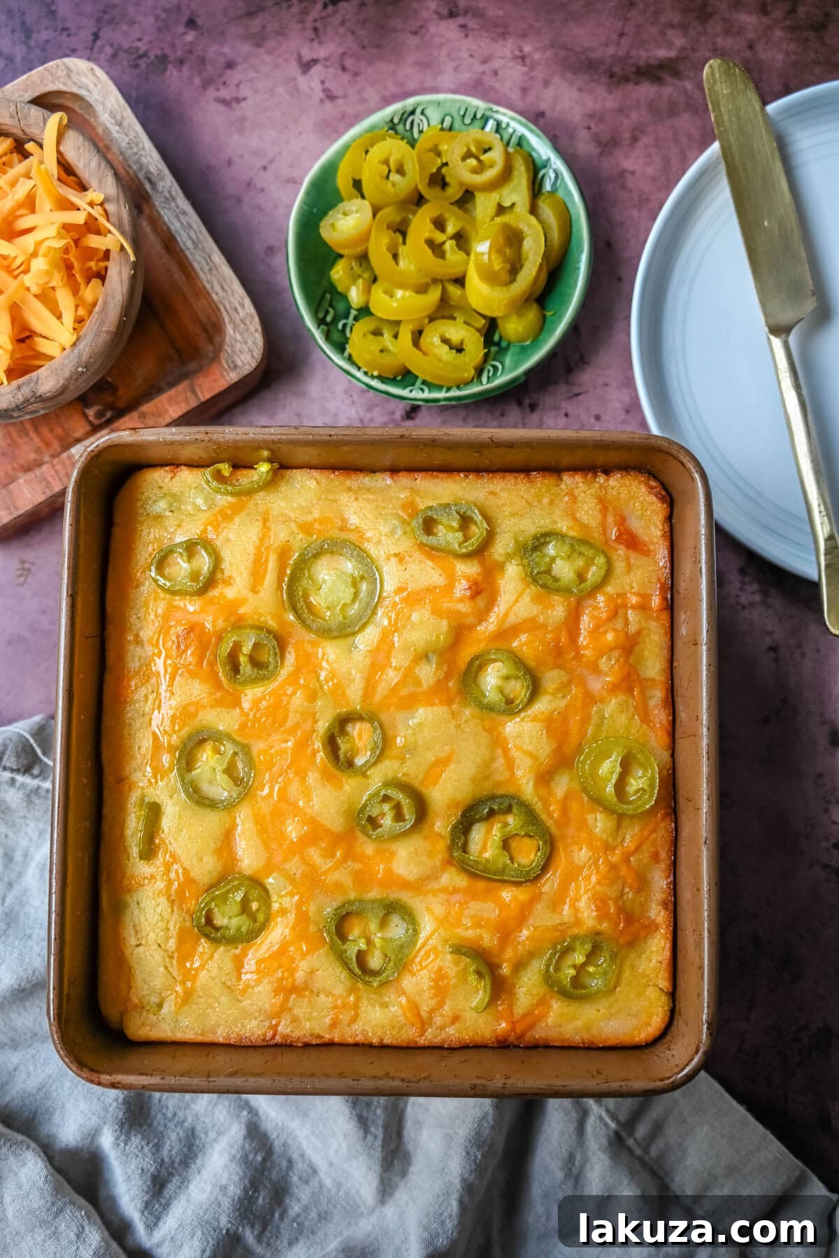 A single slice of jalapeno cheddar cornbread on a cutting board, showcasing the fluffy texture and melted cheese and jalapenos inside.