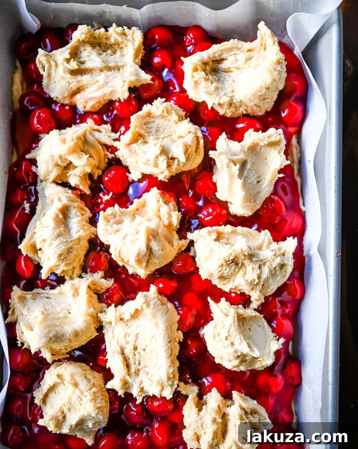 Cookie dough placed over cherry pie filling in a baking pan, ready to be baked into cherry pie cookie bars.