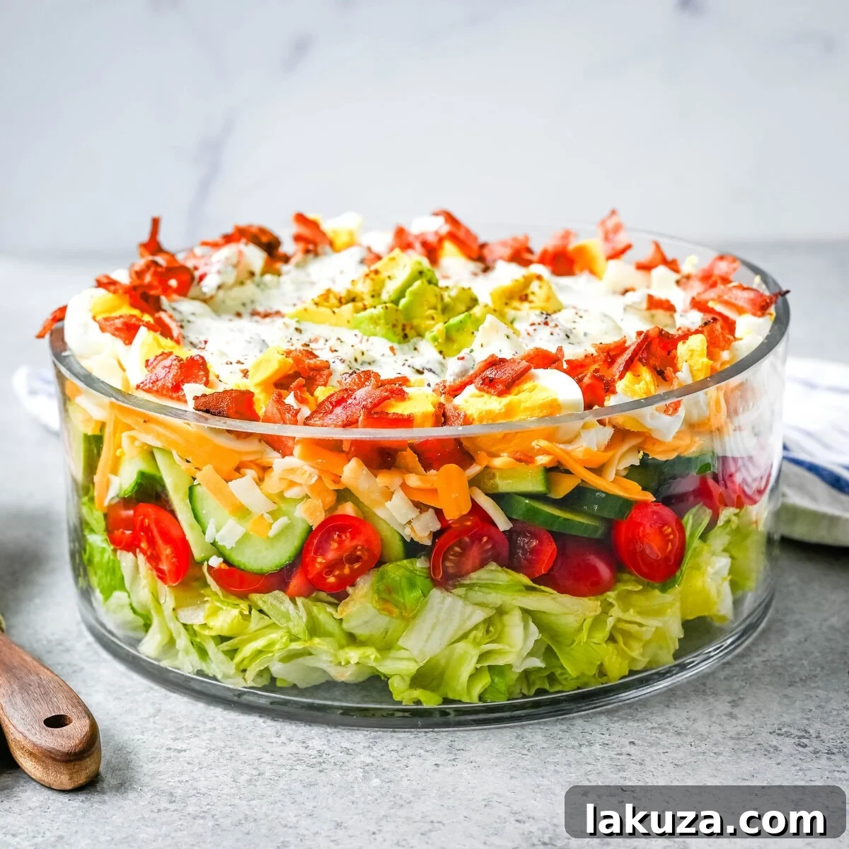 Close-up view of the vibrant layers of a seven layer salad, showcasing crisp lettuce, red tomatoes, yellow cheddar cheese, and white hard-boiled eggs in a clear bowl.