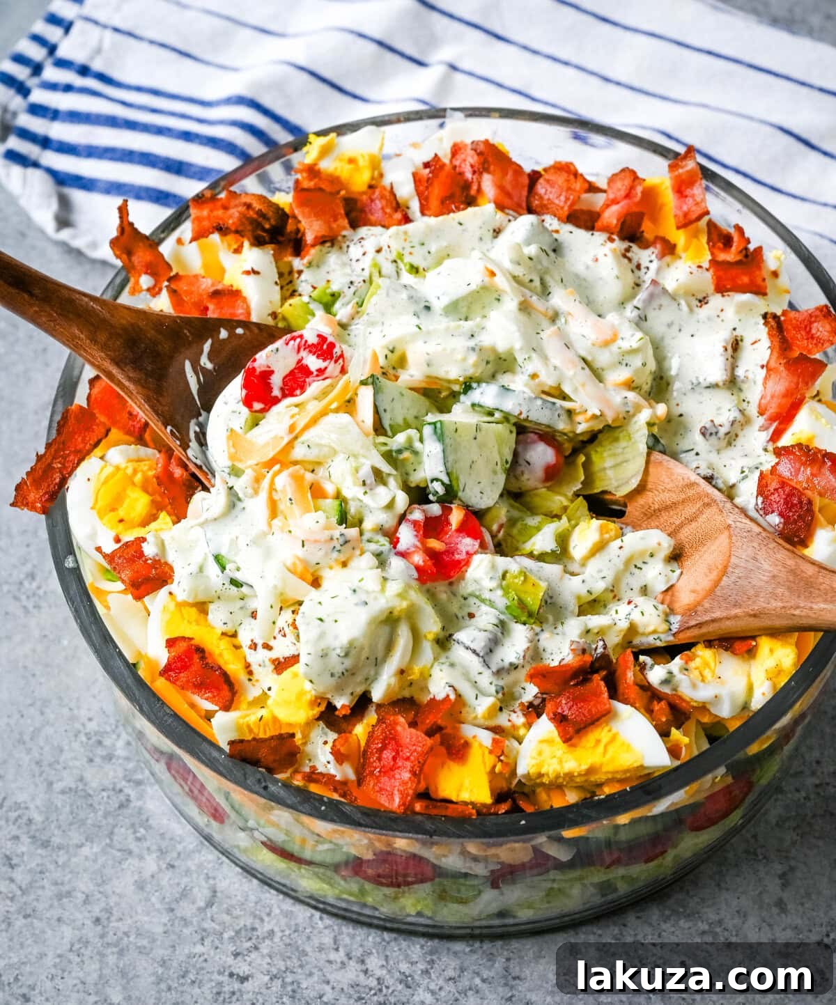 Seven layer salad ingredients being prepped on a cutting board, including diced avocado, chopped tomatoes, and shredded lettuce.