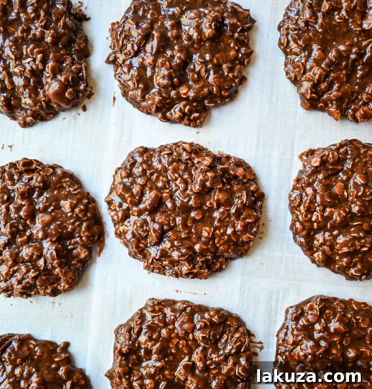 A large batch of no-bake cookies spread out on parchment paper, cooling and setting, with a spatula visible, highlighting the ease of preparation.