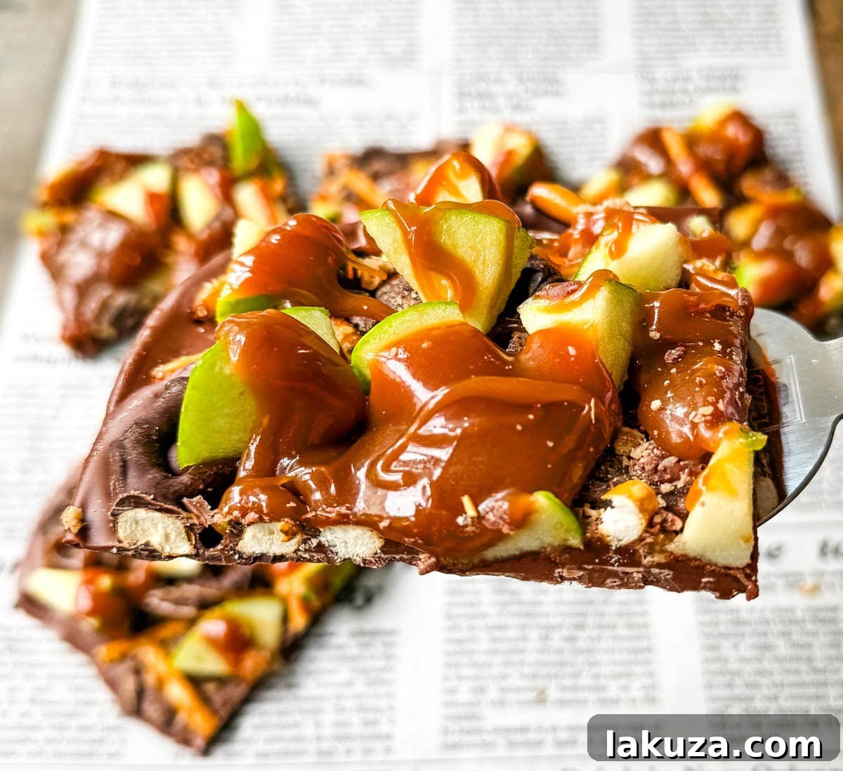 Harvest Spice Caramel Apple Bark 4 Ingredients for Caramel Apple Bark laid out: chocolate chips, pretzels, a whole Granny Smith apple, and a jar of caramel sauce, signifying readiness for preparation.