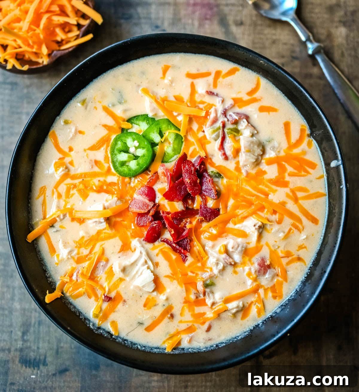 Creamy Jalapeno Chicken Bliss 2 A bowl of creamy chicken jalapeño popper soup with crispy bacon, shredded cheddar, and fresh jalapeño slices on top.