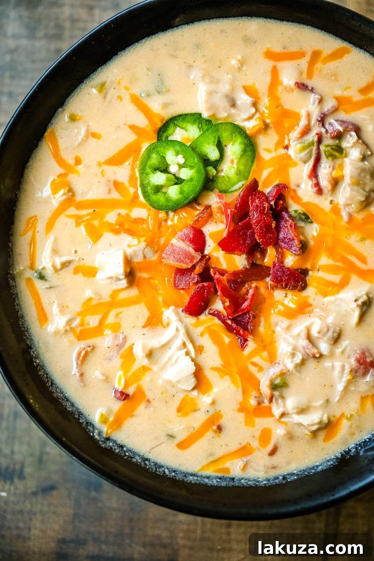 Creamy Jalapeno Chicken Bliss 4 Ingredients for creamy chicken jalapeño popper soup laid out on a wooden board, including bacon, jalapeños, onions, and cheese.