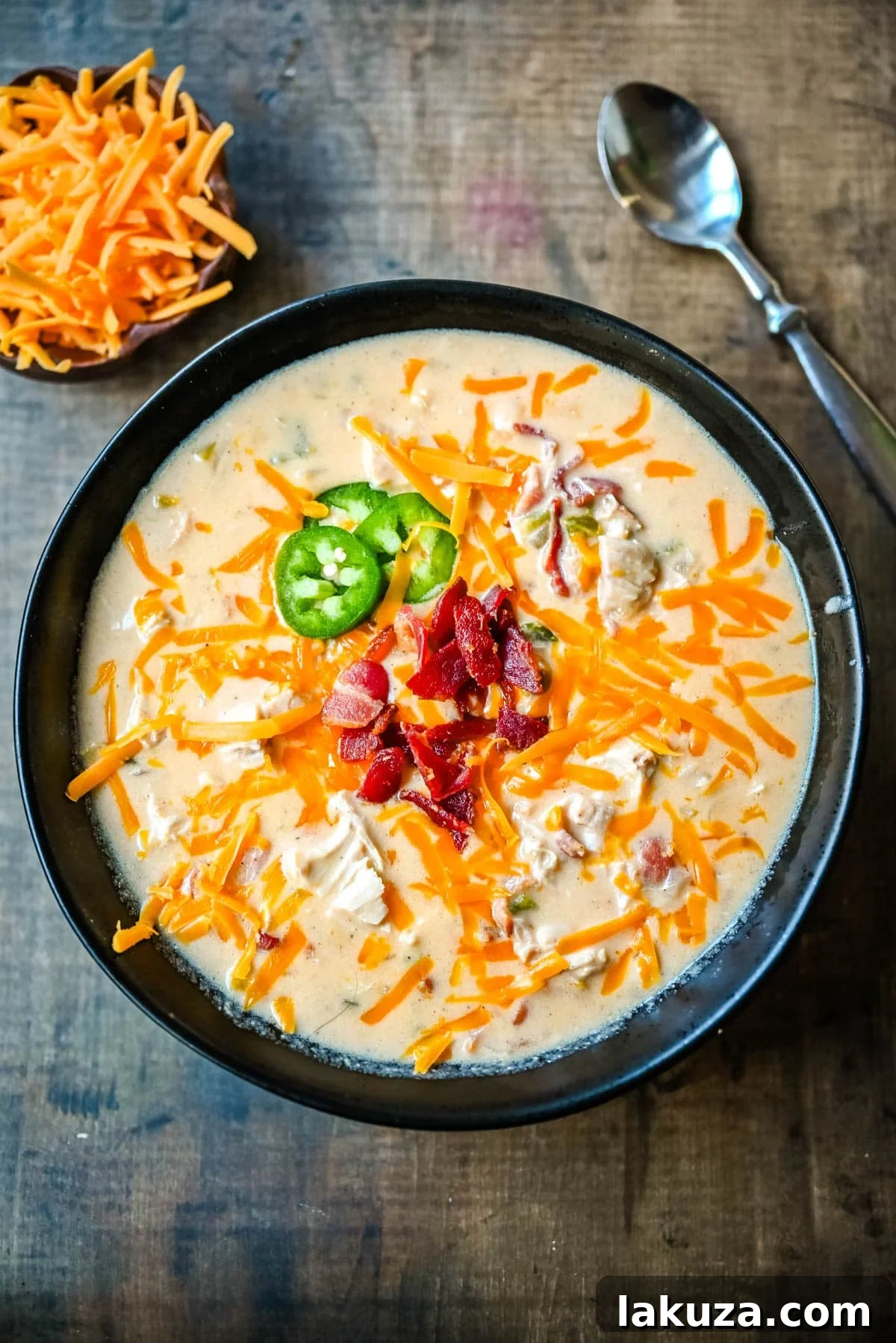 Creamy Jalapeno Chicken Bliss 5 A top-down view of a creamy chicken jalapeño popper soup bowl, garnished with melted cheese, bacon, and fresh jalapeños.