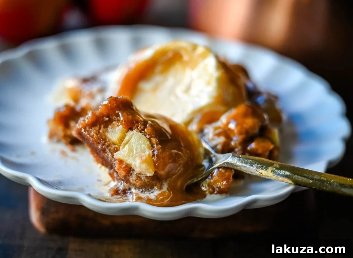 A close-up of a slice of Apple Cake with Salted Caramel, showing the moist crumb, chunks of apple, and dripping caramel sauce, with a scoop of vanilla ice cream.