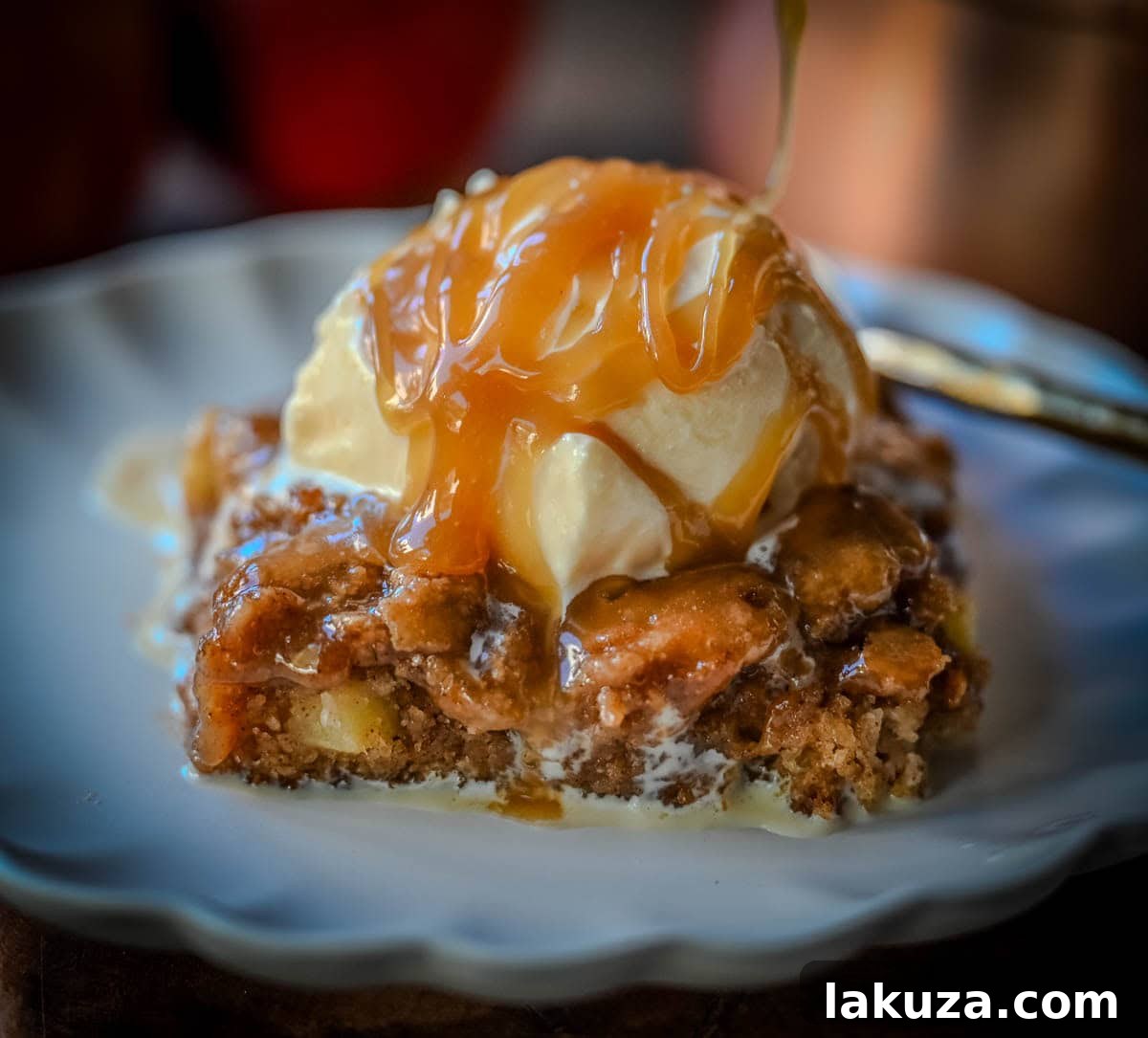 A generous serving of Apple Cake with Salted Caramel, topped with a large scoop of vanilla ice cream, on a white plate, ready to be enjoyed.