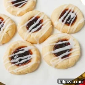 Raspberry Almond Jam Thumbprint Cookies are buttery shortbread cookies made with only butter, sugar, flour, and almond extract, topped with jam, and baked until soft and topped with homemade vanilla or almond glaze. A festive and delicious Christmas cookie recipe!