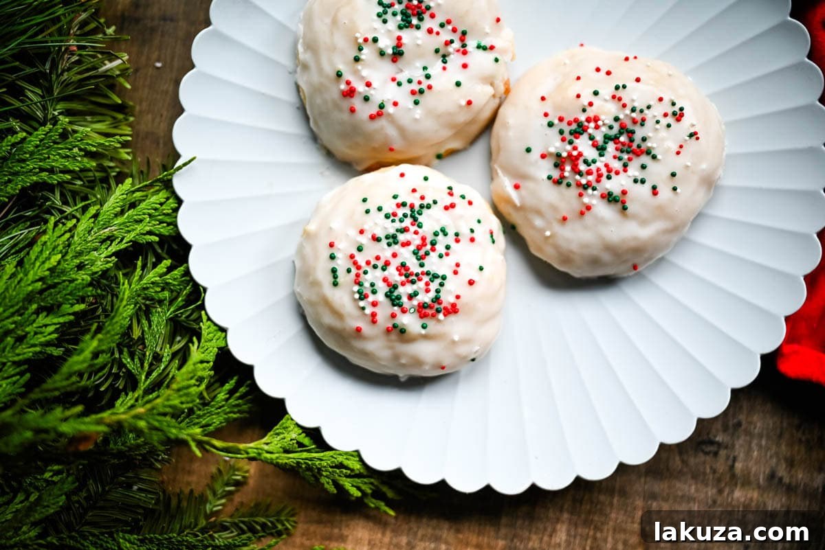 A hand gently dipping a freshly baked Italian ricotta cookie into a bowl of sweet white glaze, ready for sprinkles.