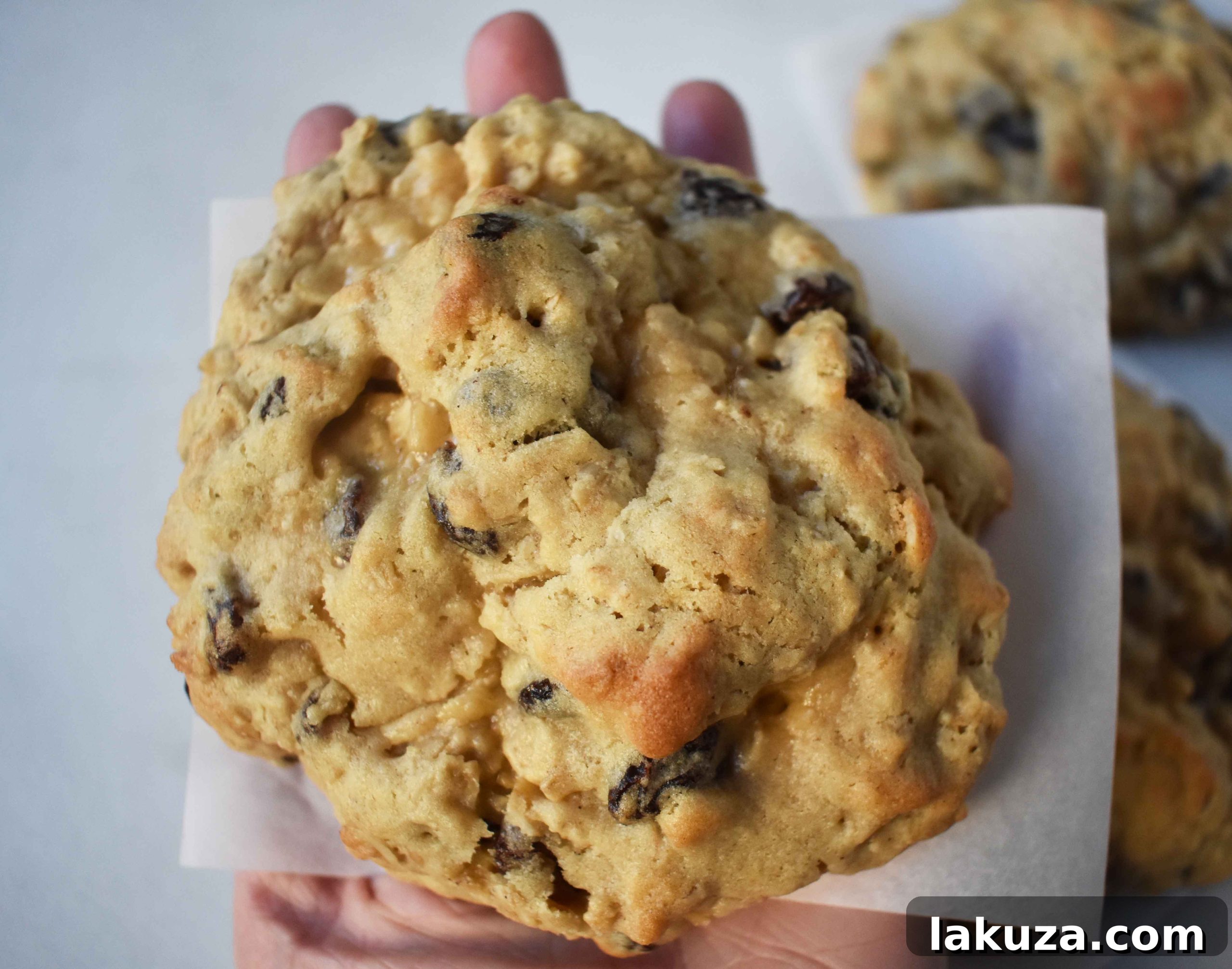 A large, rustic oatmeal raisin cookie on a wooden board, showcasing its thick and textured surface.