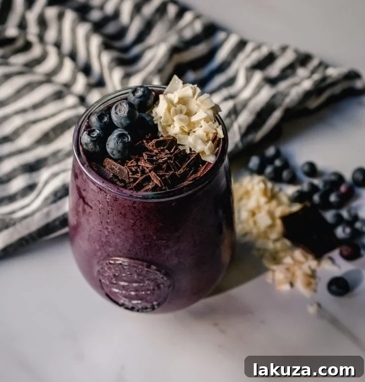 Deep Blue Cacao Dream 2 A vibrant Chocolate Blueberry Protein Smoothie in a glass, topped with fresh blueberries, almond butter drizzle, and dark chocolate shavings. It's a healthy, energizing blend perfect for breakfast or a snack.