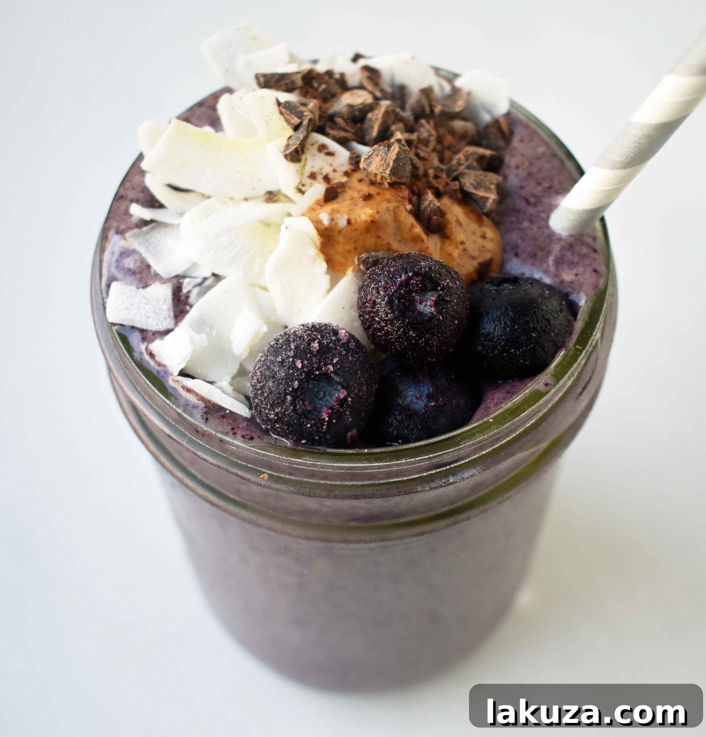 Deep Blue Cacao Dream 4 An overhead shot of a Wild Blueberry Chocolate Coconut Smoothie, garnished beautifully with fresh blueberries, a generous swirl of almond butter, and fine dark chocolate shavings. This photograph highlights the appealing presentation of the nutritious, crave-worthy shake.