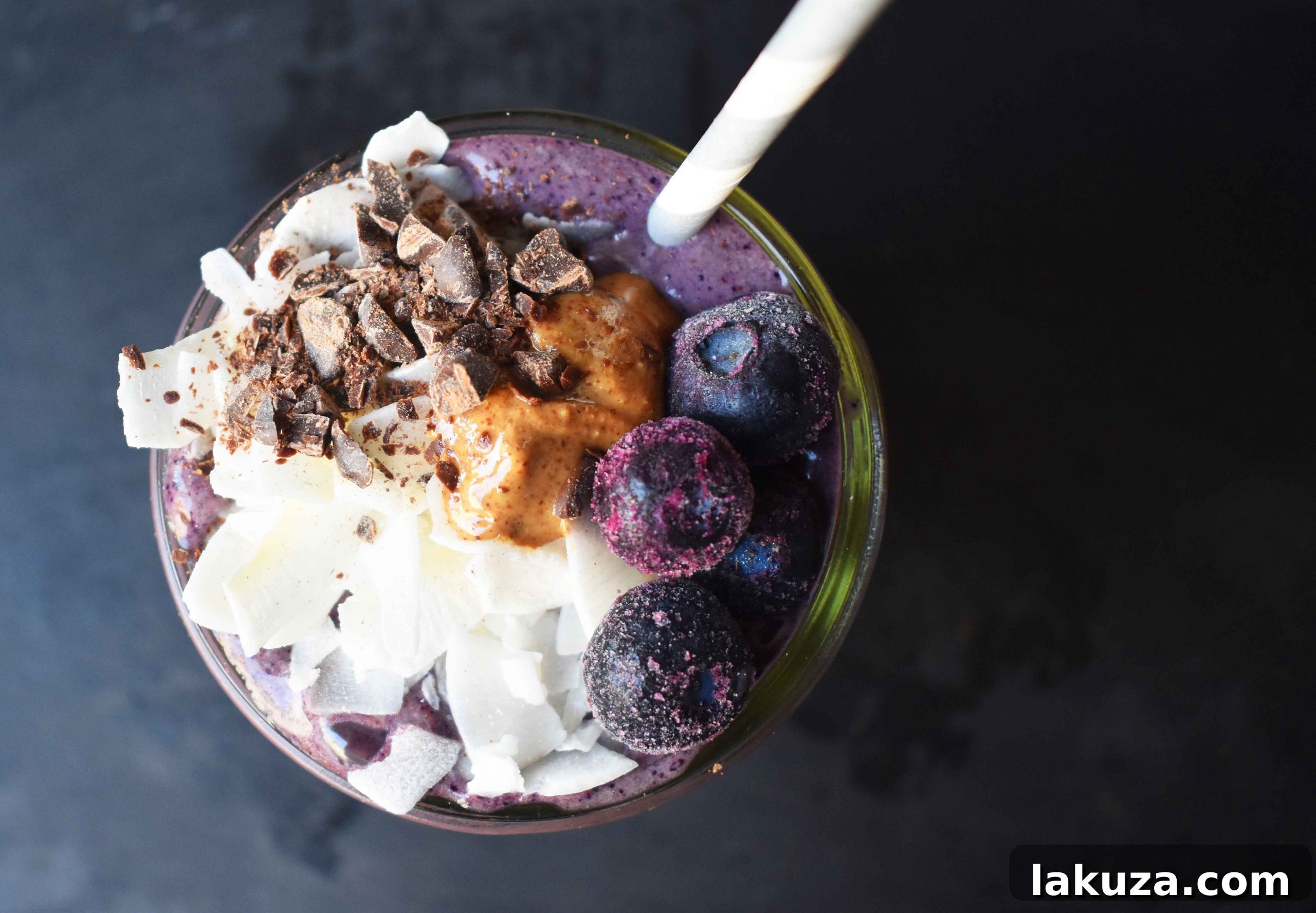Deep Blue Cacao Dream 5 A refreshing Wild Blueberry Chocolate Coconut Smoothie in a tall glass, garnished with fresh blueberries and a drizzle of almond butter. This image emphasizes the drink's natural, wholesome appeal and its delicious presentation, perfect for a healthy start to the day.
