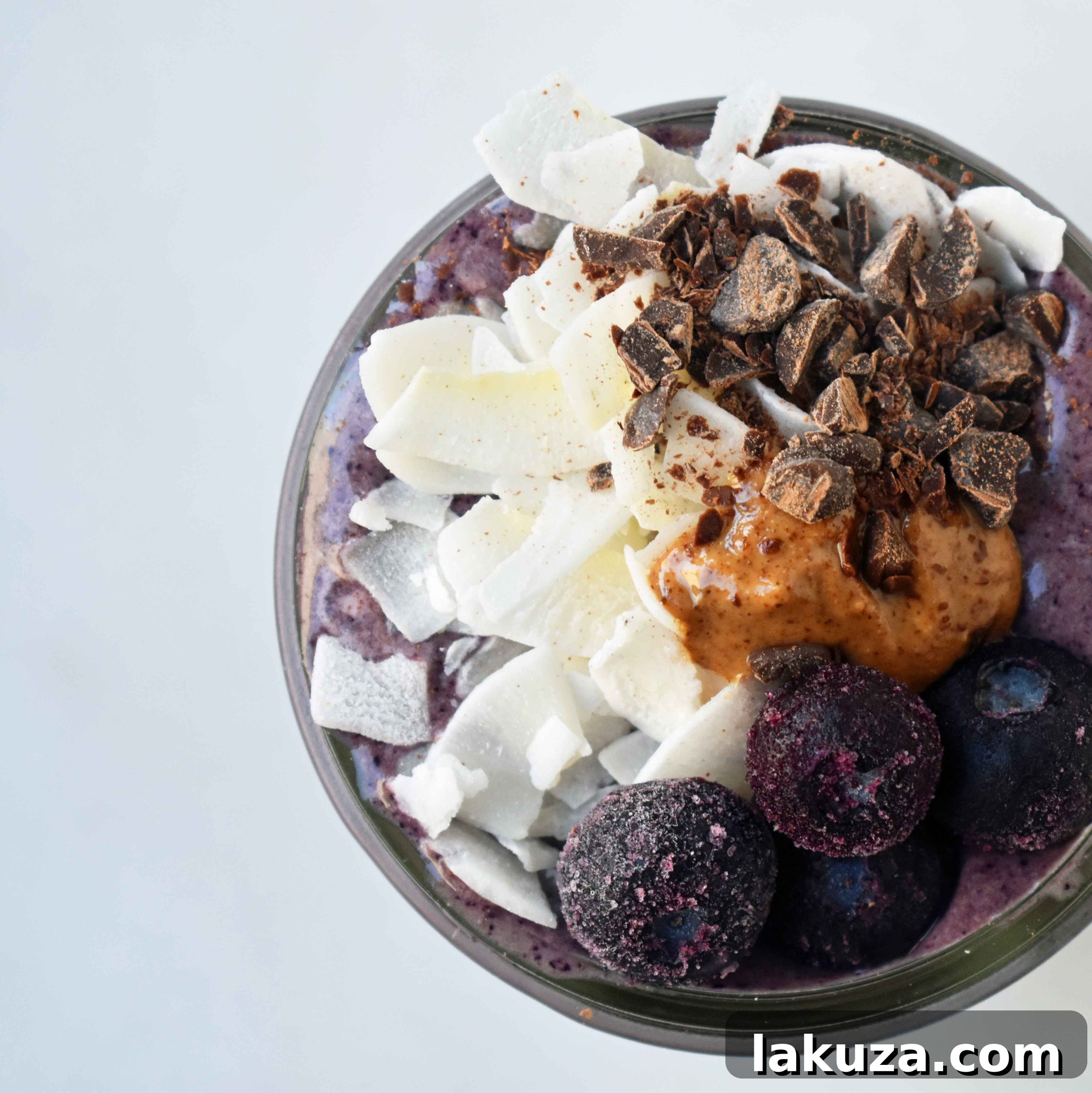 Deep Blue Cacao Dream 6 A top-down view of a glass of Wild Blueberry Chocolate Coconut Smoothie, showing the generous toppings of fresh blueberries, creamy almond butter, and delicate dark chocolate shavings. The presentation is enticing and emphasizes the rich texture of the protein shake.