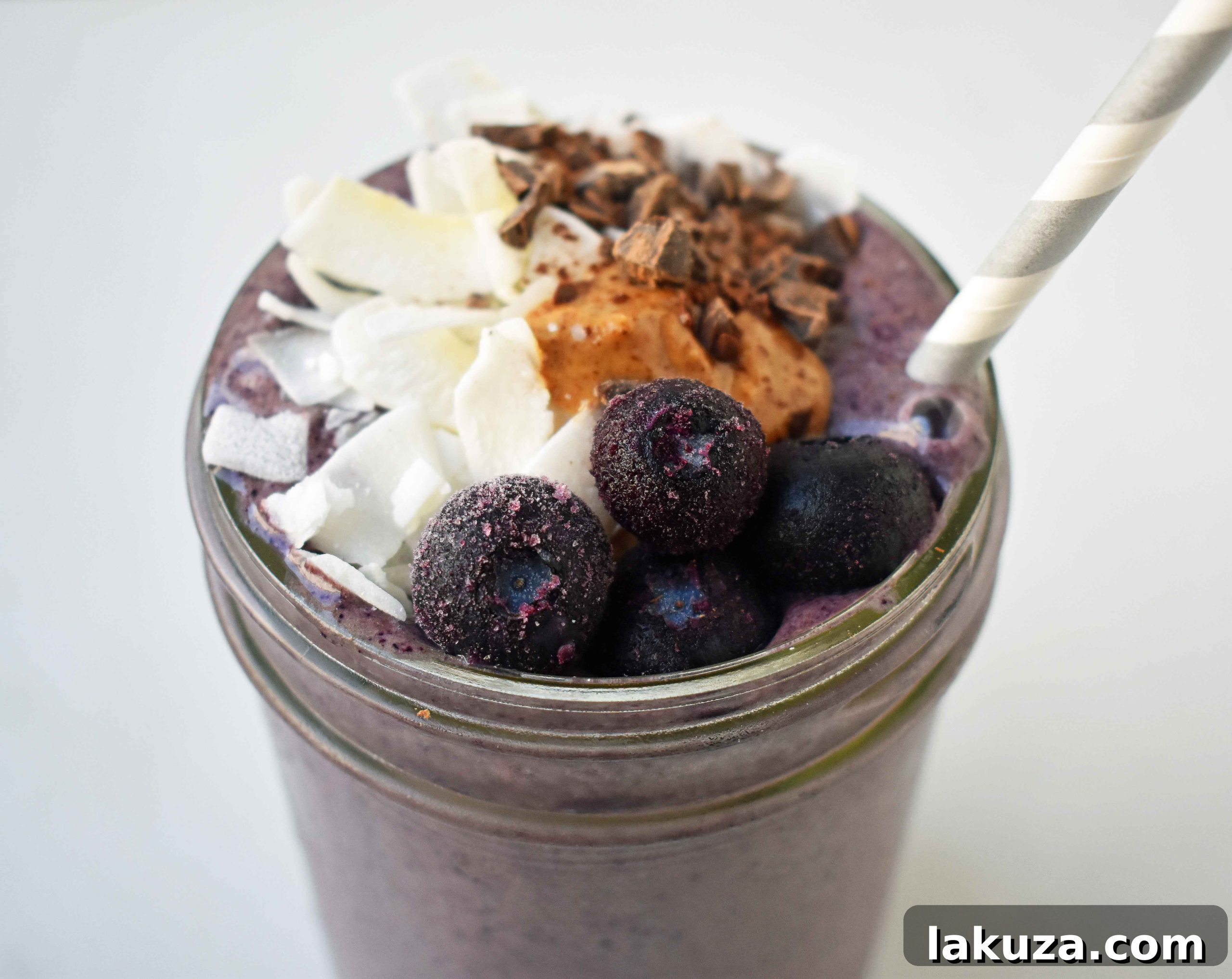 Deep Blue Cacao Dream 8 A tall glass of Wild Blueberry Chocolate Coconut Smoothie, freshly blended and topped with a sprinkle of blueberries. The smooth, inviting texture promises a delicious and healthy treat. This smoothie is made with chocolate protein, coconut milk, and almond butter.
