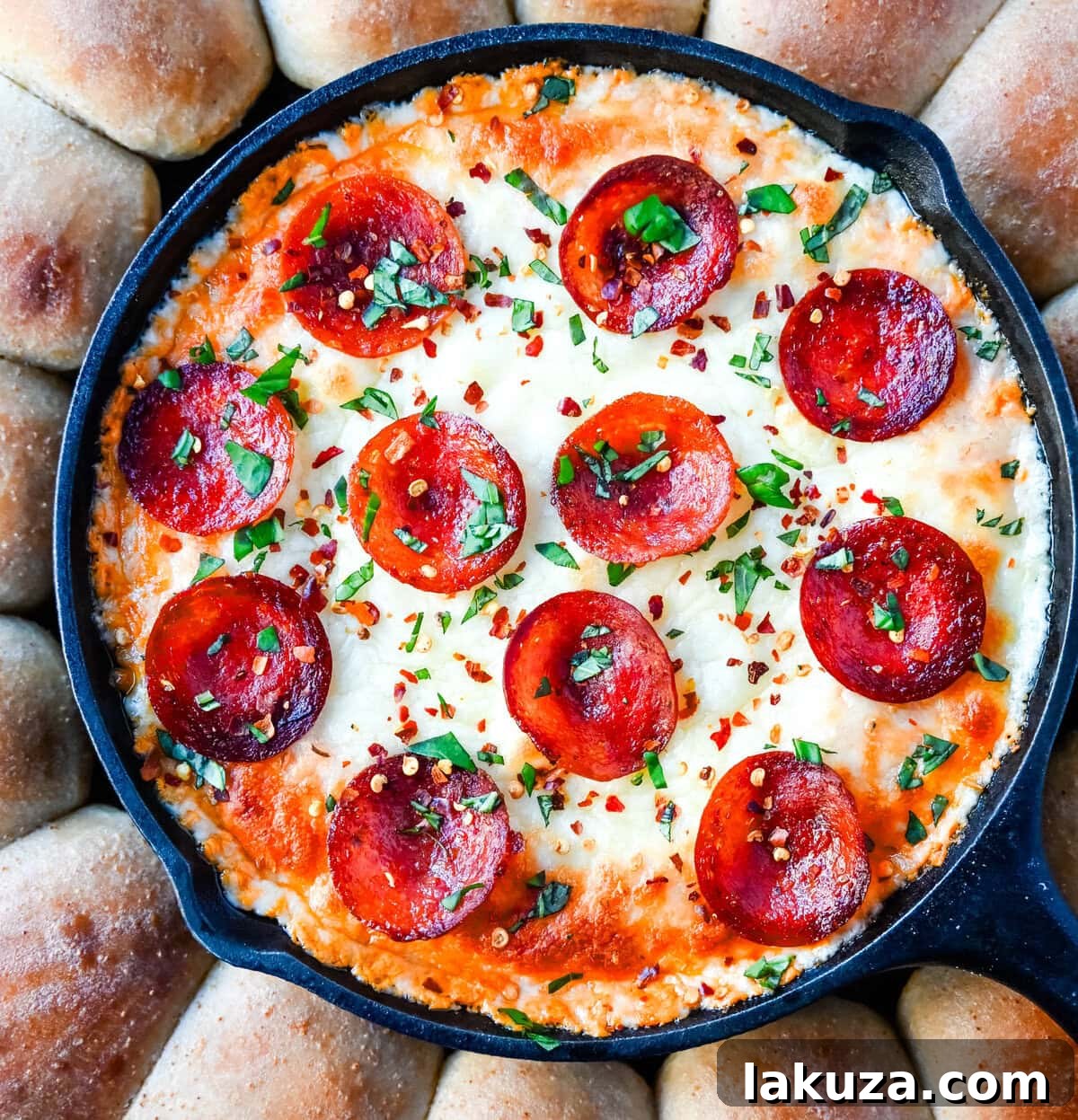 A spoon scooping a generous portion of bubbly Hot Pepperoni Pizza Dip from a cast iron skillet, with golden pizza dippers around the edge.