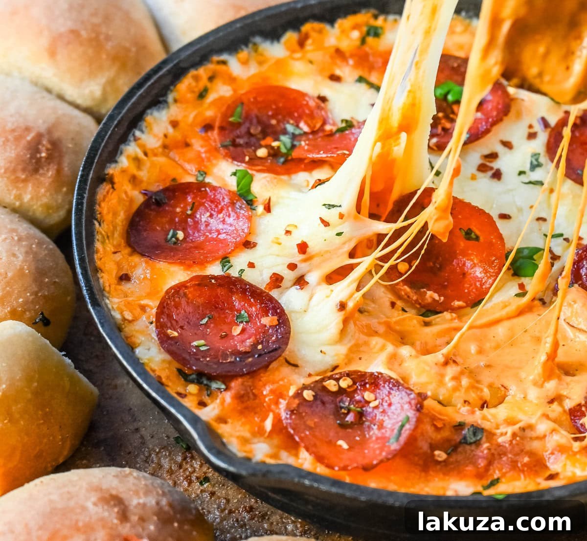 A top-down view of the Hot Pepperoni Pizza Dip in a skillet, garnished with fresh basil, surrounded by various dippers like bread rolls and vegetables.