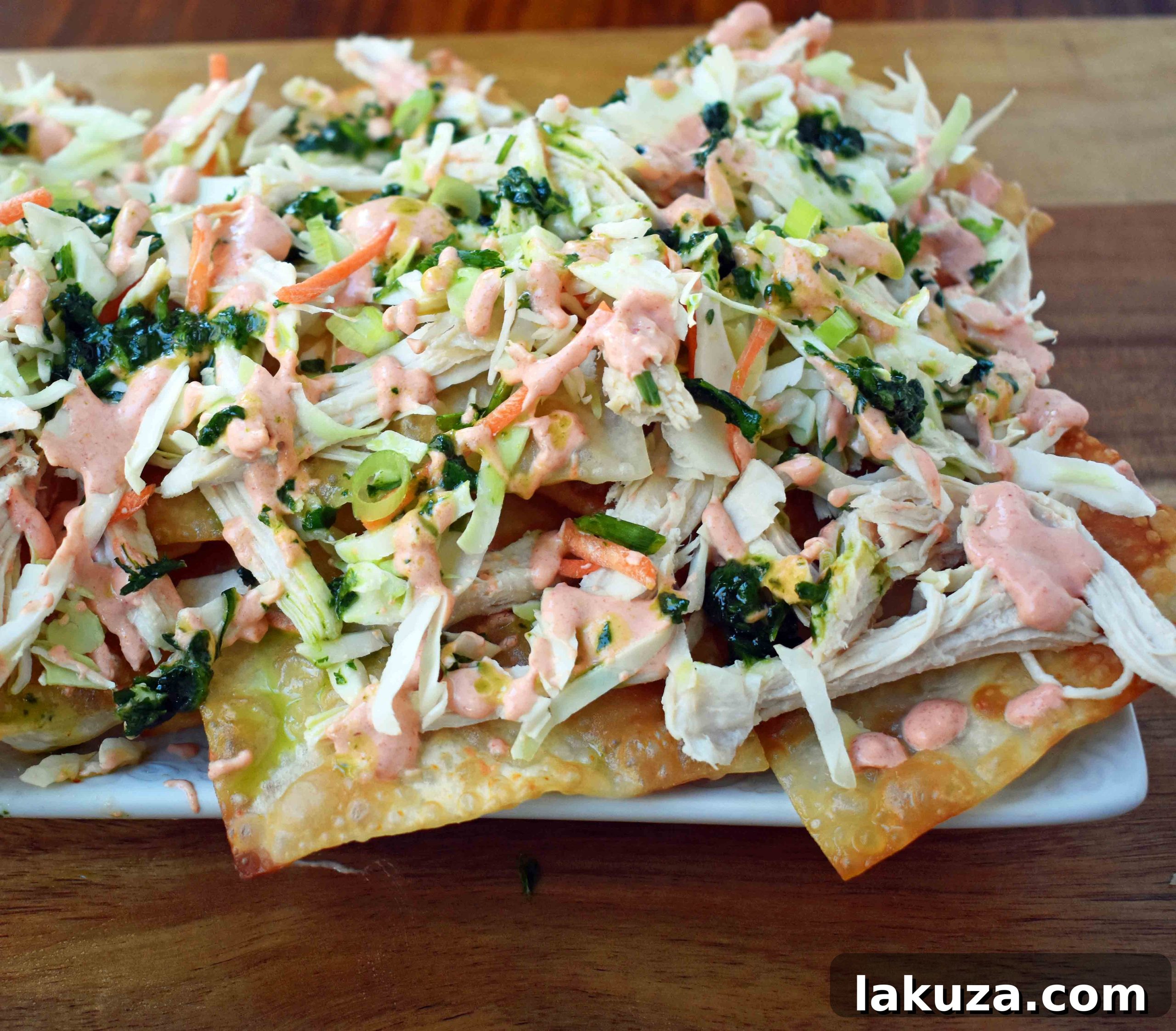 Asian Wonton Chicken Nachos. Fried wontons, pulled chicken, sriracha cream, cabbage mix, and sweet cilantro sauce. An Asian twist on nachos for the perfect party appetizer.