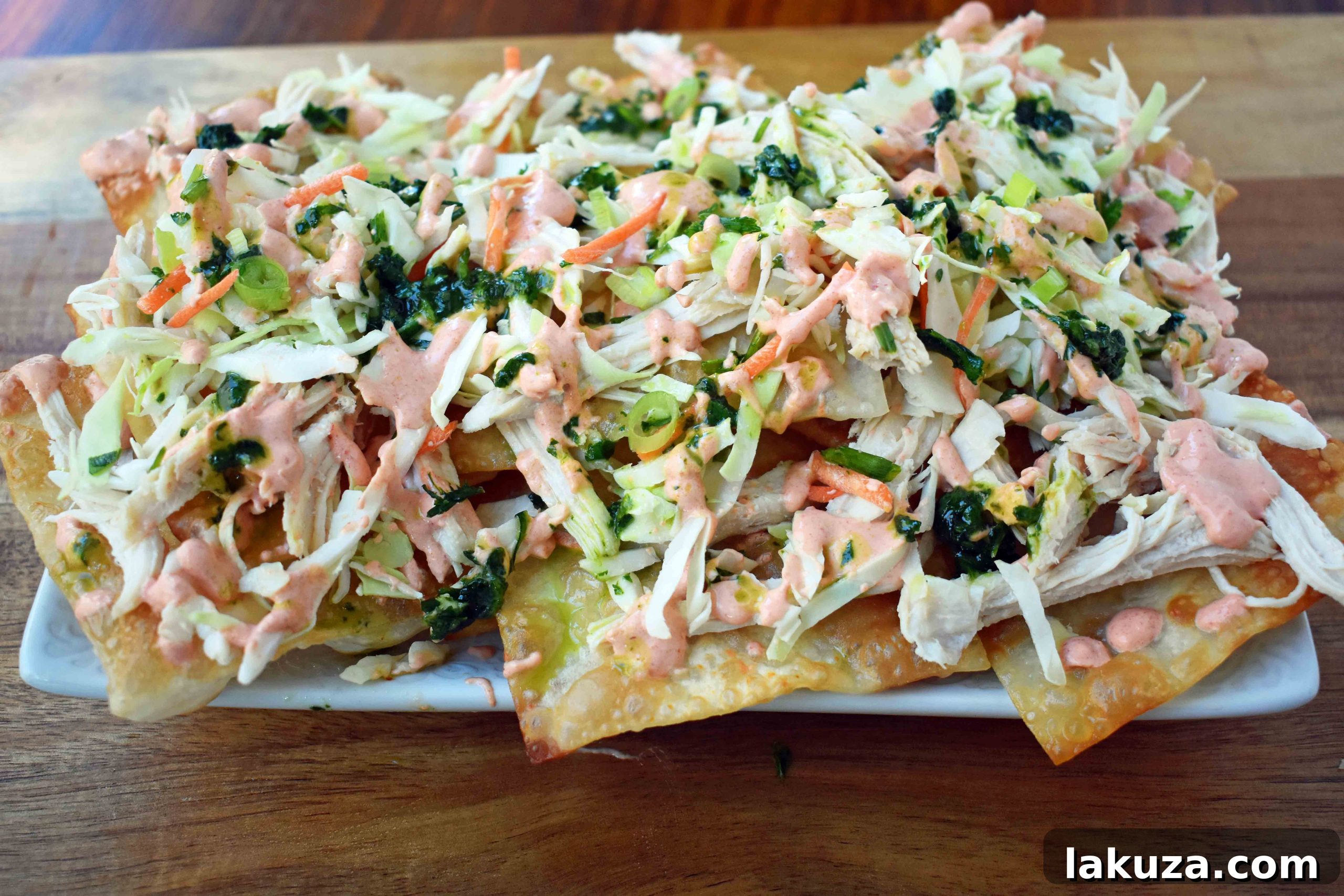 Asian Wonton Chicken Nachos. Fried wontons, pulled chicken, sriracha cream, cabbage mix, and sweet cilantro sauce. An Asian twist on nachos for the perfect party appetizer.
