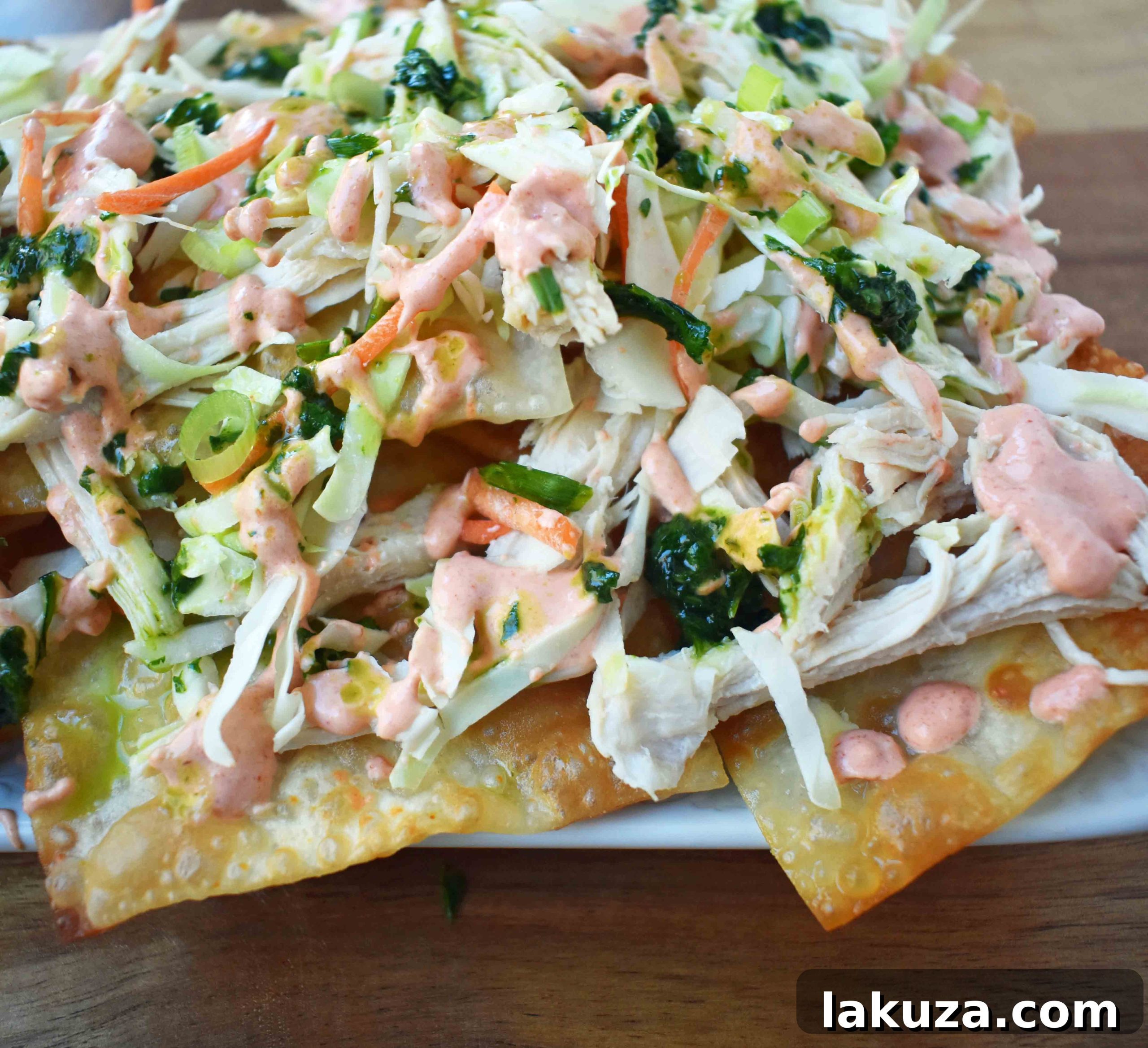 Asian Wonton Chicken Nachos. Fried wontons, pulled chicken, sriracha cream, cabbage mix, and sweet cilantro sauce. An Asian twist on nachos for the perfect party appetizer.