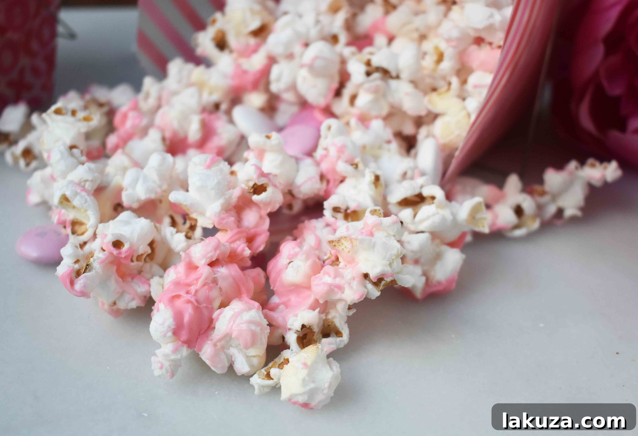 Irresistible Valentine White Chocolate M&M Popcorn 4 The process of making Valentine's White Chocolate M & M Popcorn, with melted chocolate being drizzled over freshly popped corn.
