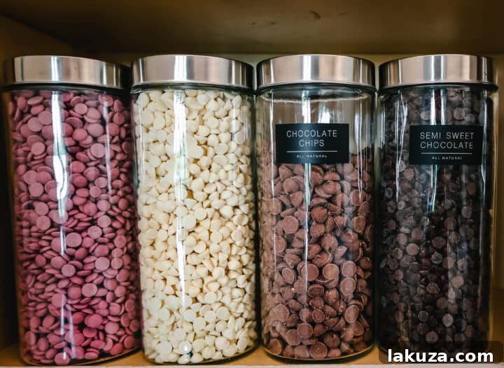 Close-up of glass jars filled with different types of chocolate chips: semi-sweet, white, milk, and ruby, neatly arranged in a baking center.