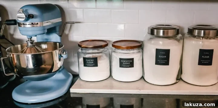 A row of neatly labeled glass jars filled with various baking ingredients, showcasing elegant black and white labels.