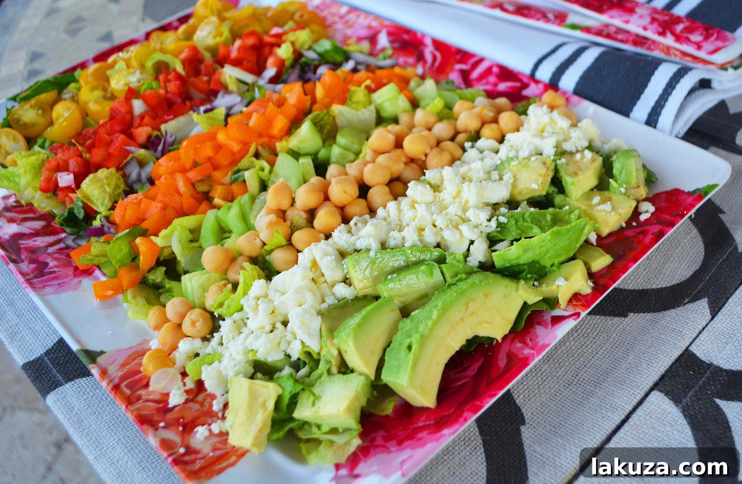 A beautifully arranged Color Me Pretty Greek Salad, showcasing a rainbow of fresh vegetables, creamy feta, and garbanzo beans, drizzled with a homemade Greek dressing.