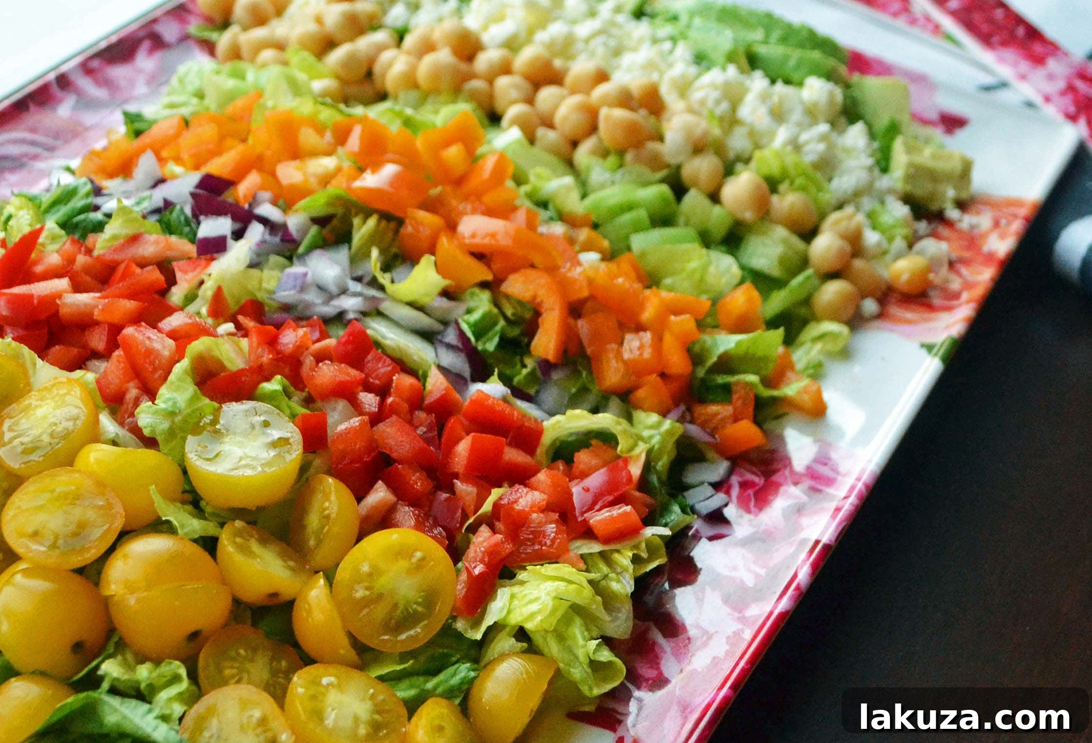 A close-up of a refreshing Greek Salad featuring crisp lettuce, chickpeas, ripe avocado, vibrant tomatoes, and crumbled feta cheese, dressed with a homemade vinaigrette.