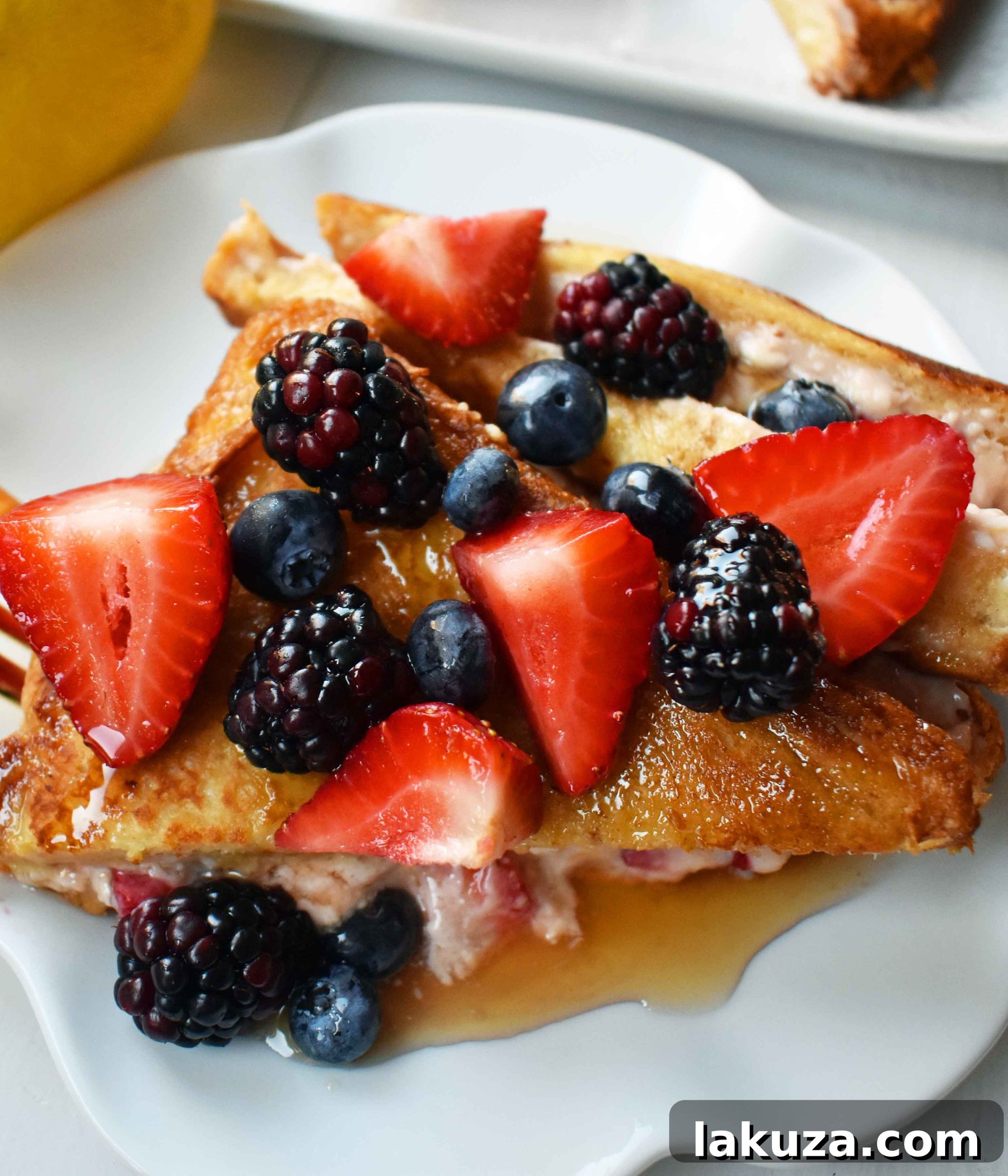 Pile of Strawberries and Cream Stuffed French Toast pieces, garnished with powdered sugar and berries.