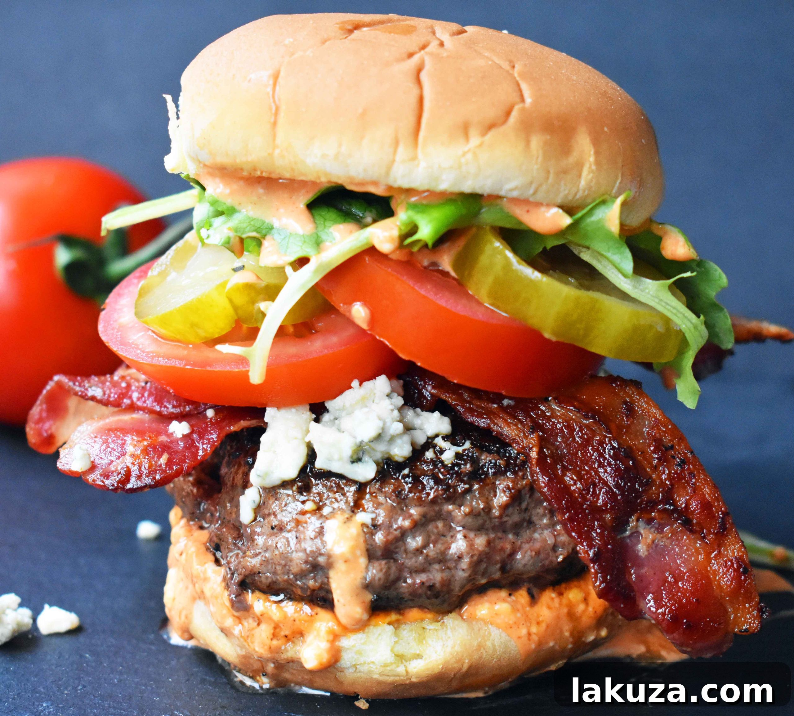 The Wyrmbane Burger 2 Dragonslayer Burger. Beef with blue cheese, crispy bacon, juicy tomatoes, crunchy pickles, spring mix, and buffalo ranch sauce. A gourmet burger experience.