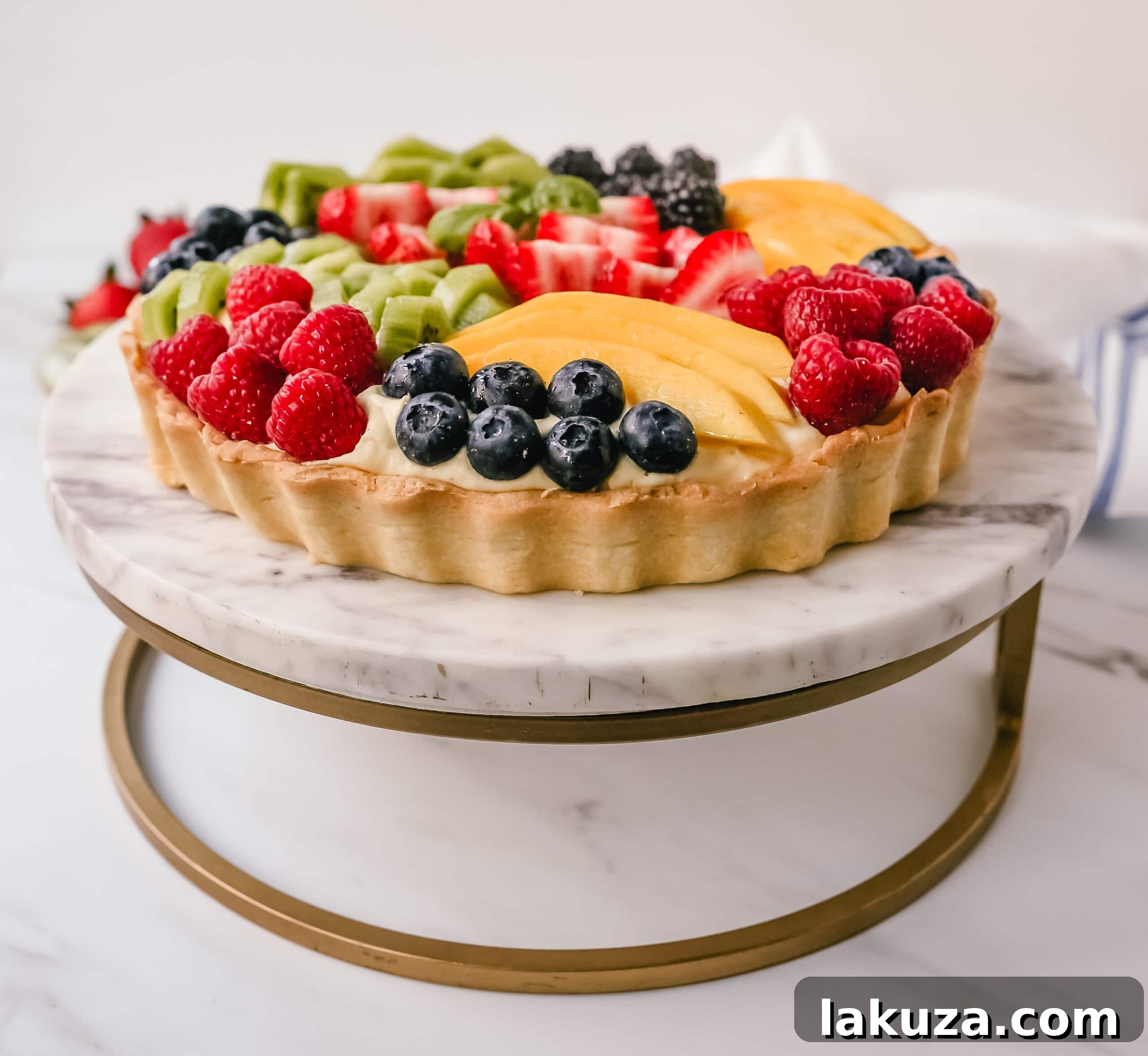 Hand carefully arranging colorful fresh fruits like berries, kiwi, and mango slices onto a creamy fruit tart.