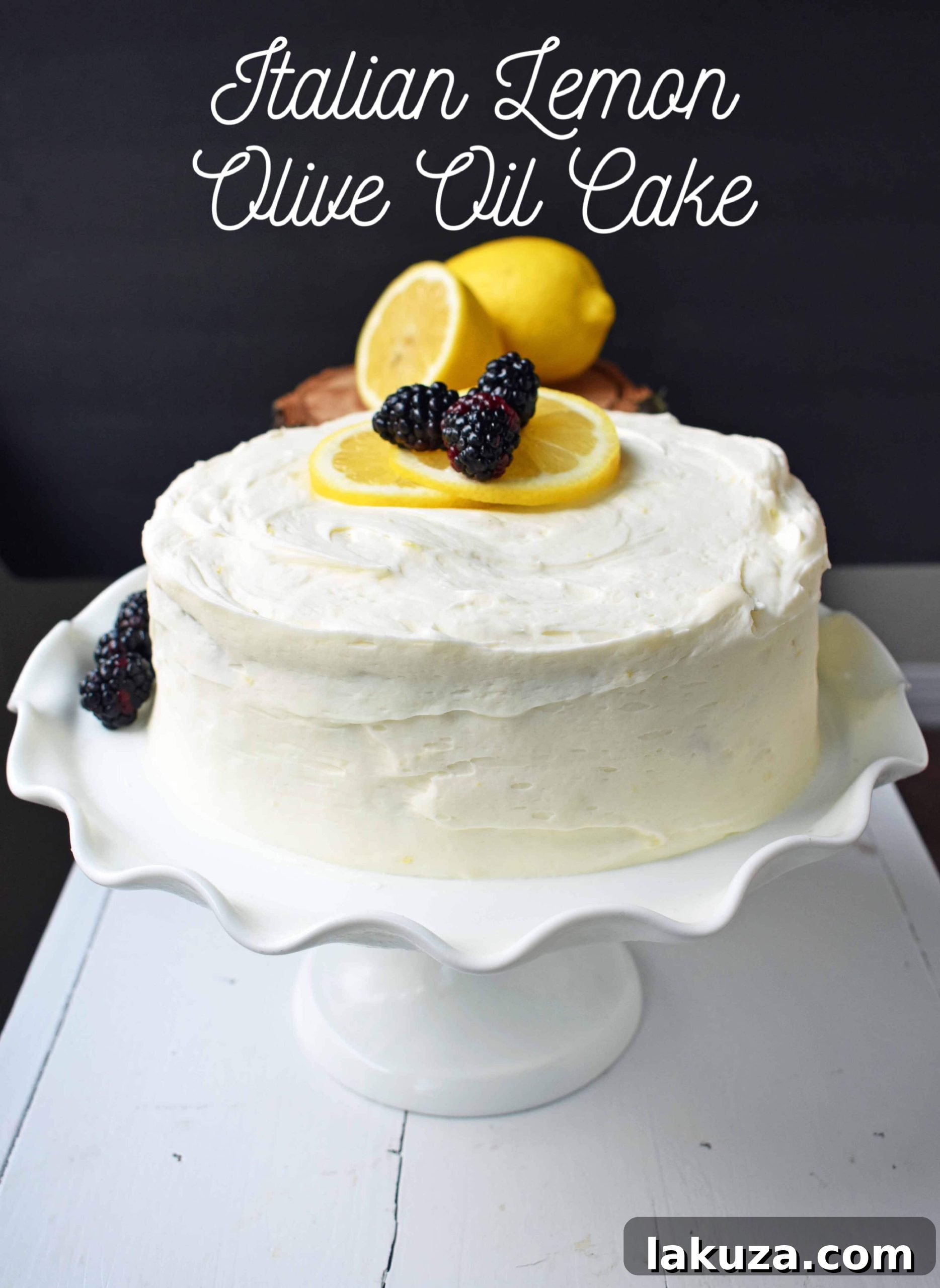 A grand, multi-layered Italian Lemon Olive Oil Cake, exquisitely decorated with fresh lemons, mint, and berries, positioned on a large wooden board.