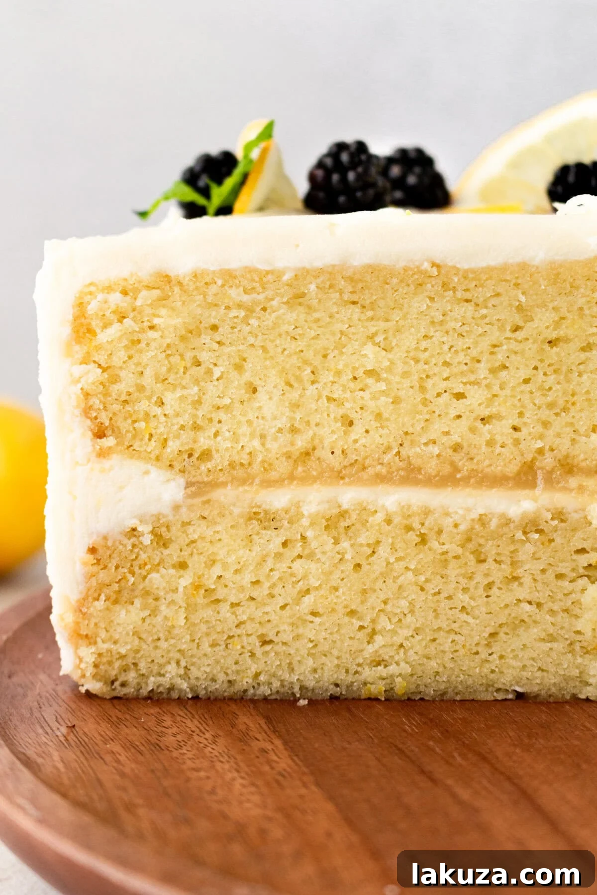 A two-layer Lemon Olive Oil Cake generously covered with lemon vanilla cream cheese frosting, awaiting final garnishes.