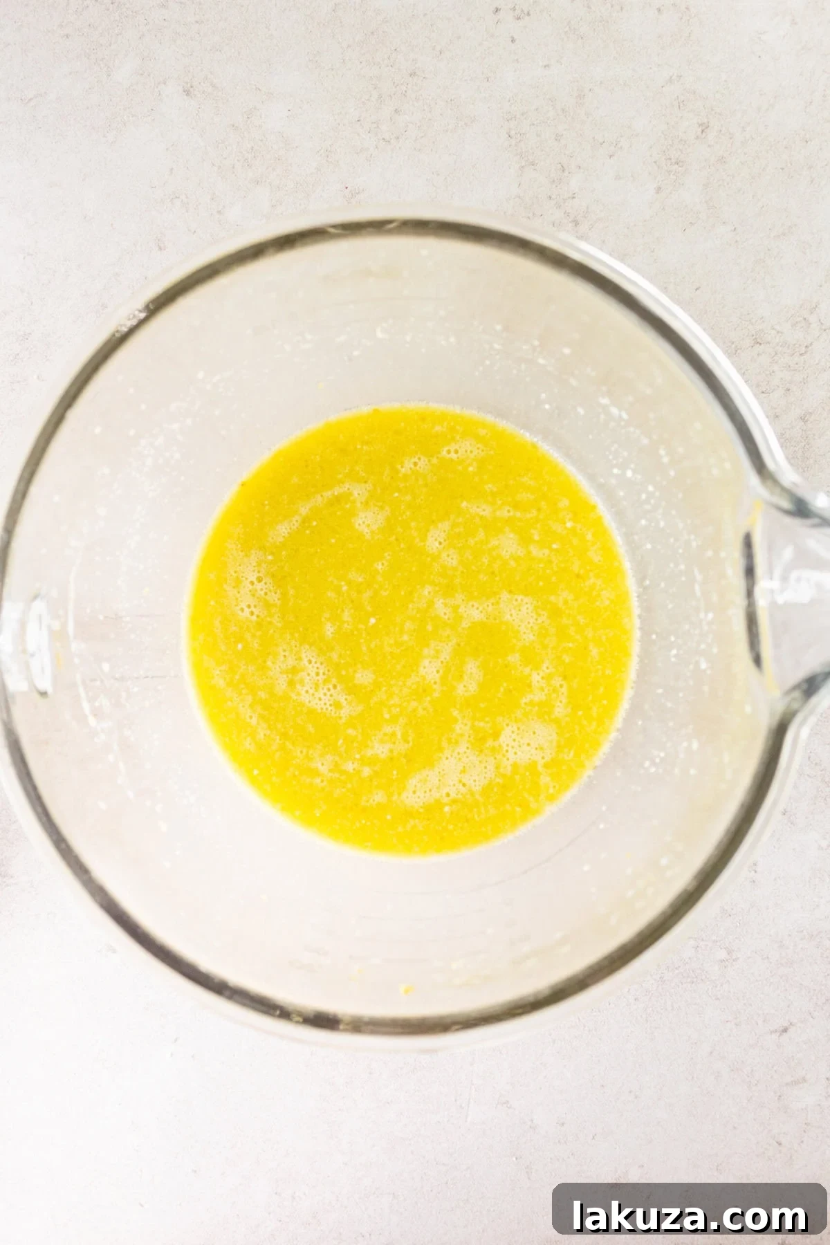 A mixing bowl filled with wet ingredients for lemon olive oil cake batter, including oil, eggs, milk, lemon juice, and zest.