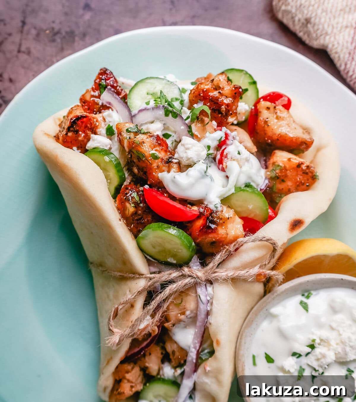 Close-up of a homemade Greek Chicken Gyro with grilled chicken, tzatziki, and fresh vegetables spilling out of a warm pita bread.